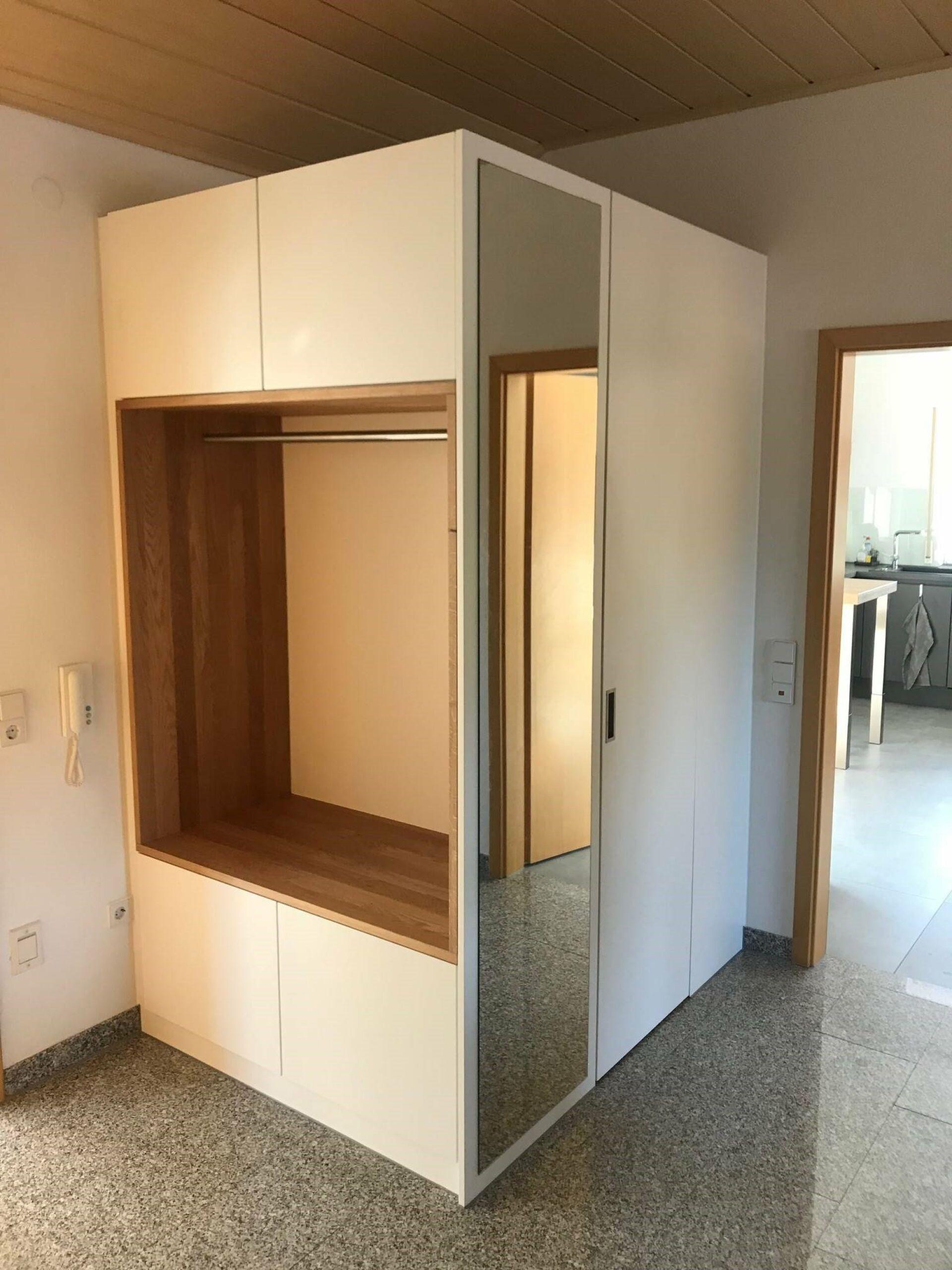 Maßgefertigte Einbaugarderobe in Weiß mit integriertem Spiegel, Kleiderstange und Stauraum unter Dachschräge auf Steinboden.