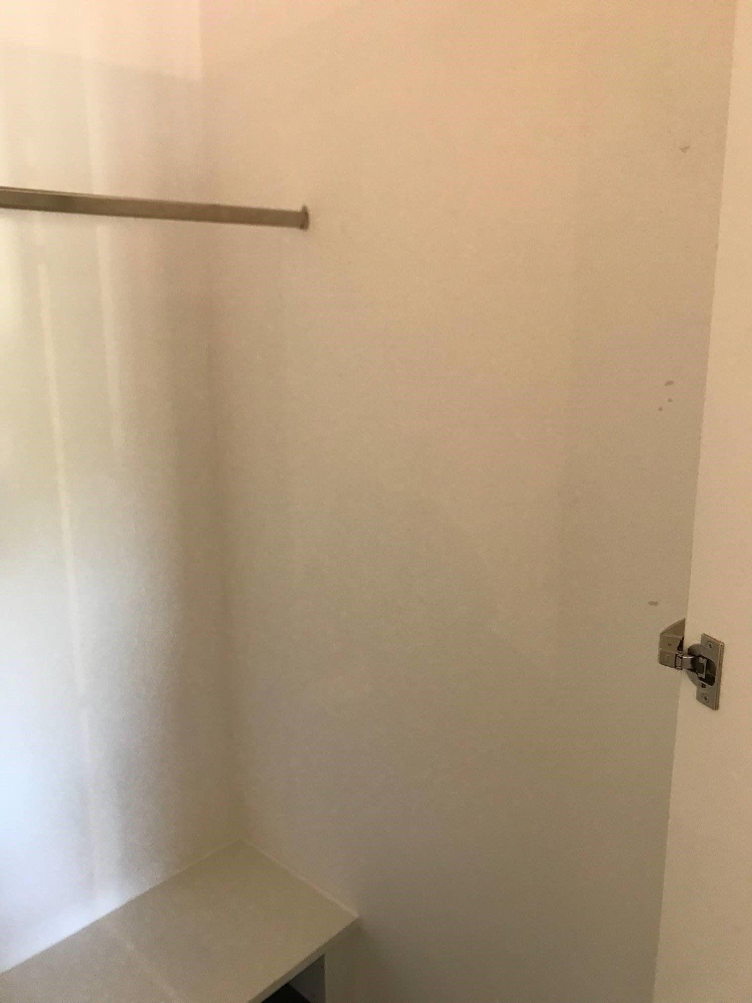 Geöffneter weißer Kleiderschrank mit Kleiderstange, leerer Innenraum und sichtbaren Scharnieren.