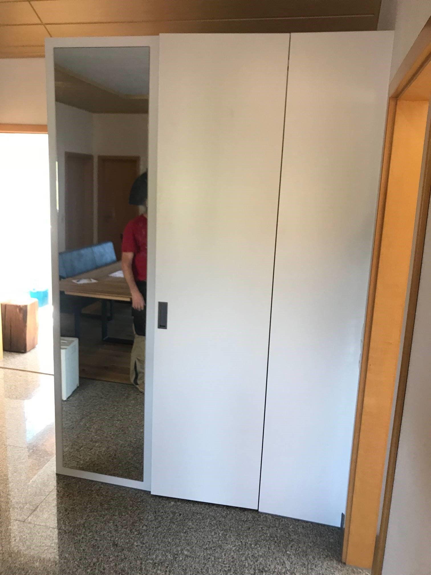Weiße Garderobe mit integriertem Spiegel, Person im Hintergrund sichtbar durch die Spiegeltür.