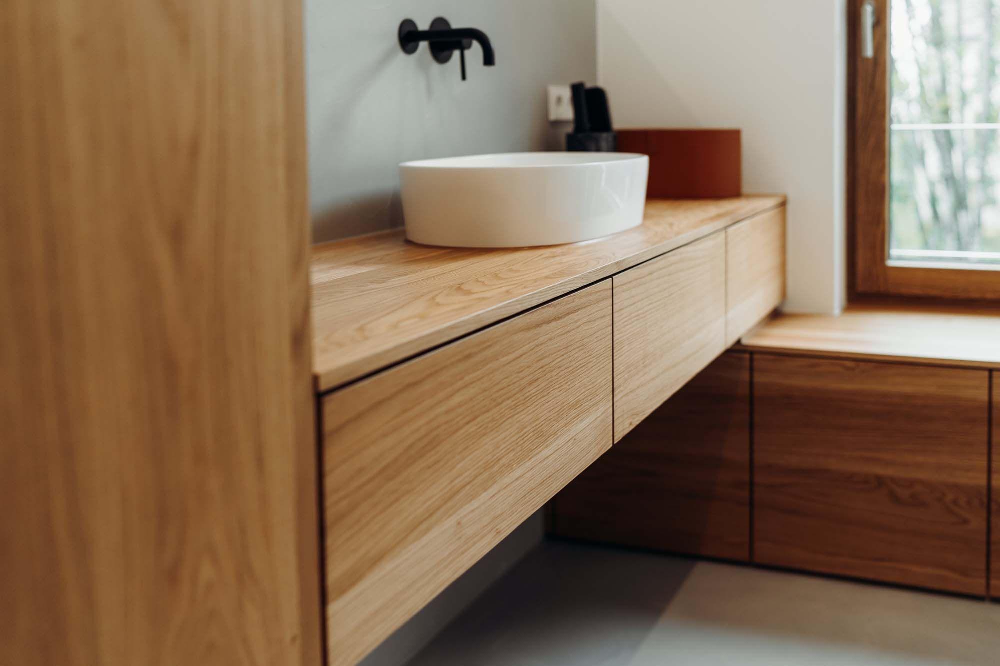  Modernes Badezimmer mit schwebender Holzwaschtischplatte, rundem weißen Aufsatzwaschbecken, schwarzer Wandarmatur und Holzfenstern.