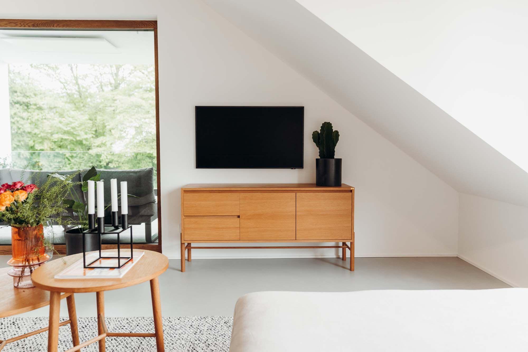 Wohnzimmer-Detail mit Holz-TV-Möbel, schwarzem Fernseher, Kaktus in schwarzem Topf, rundem Couchtisch mit Kerzen und Blumenvase.