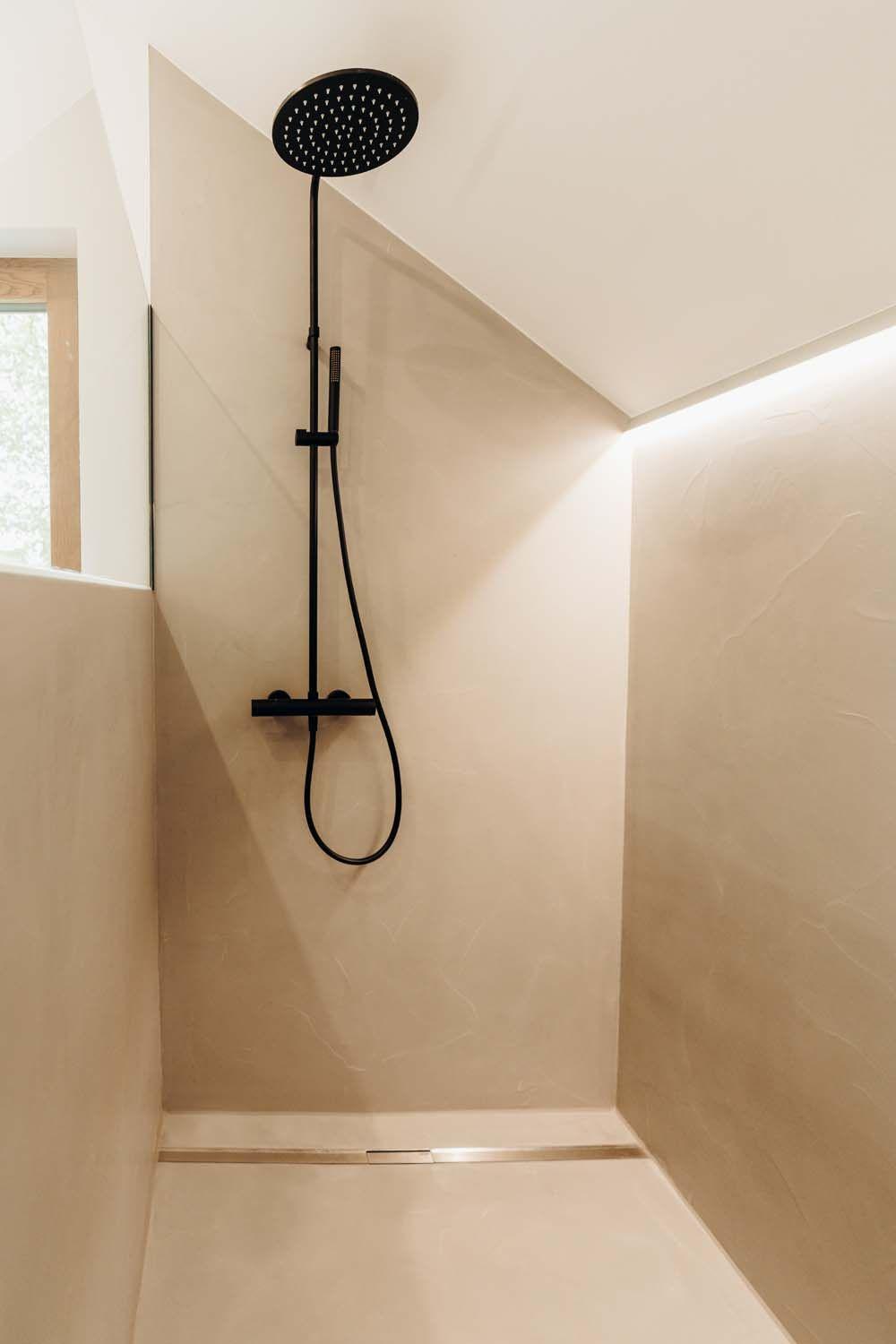Moderne begehbare Dusche mit schwarzer Regenduscharmatur, beigefarbenen Wandfliesen, Glasabtrennung und indirekter LED-Beleuchtung unter der Dachschräge.