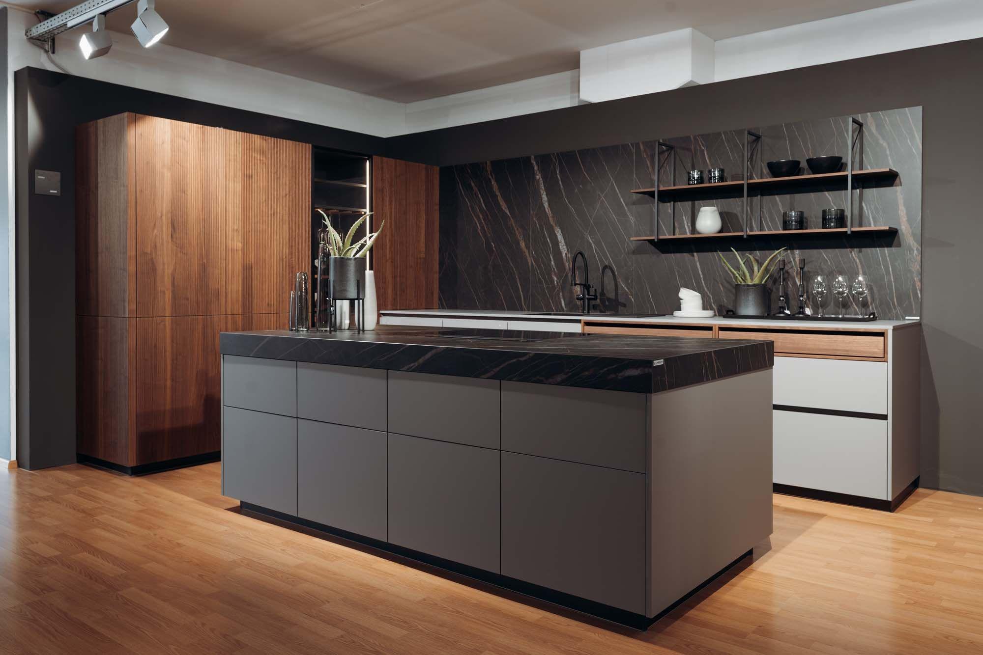 Moderne Designer-Küche mit grauer Kochinsel, schwarzer Marmorarbeitsplatte, Holzfronten, dunkler Naturstein-Rückwand und schwimmenden Regalen auf Parkettboden.