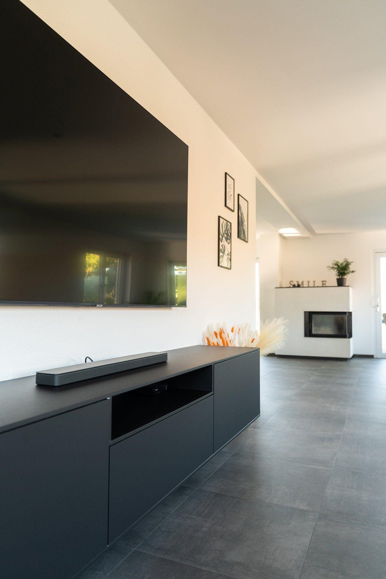 Moderner TV-Bereich mit anthrazitfarbenem Lowboard, Wandfernseher, Bildergruppe an der Wand und Pampasgras-Dekoration.