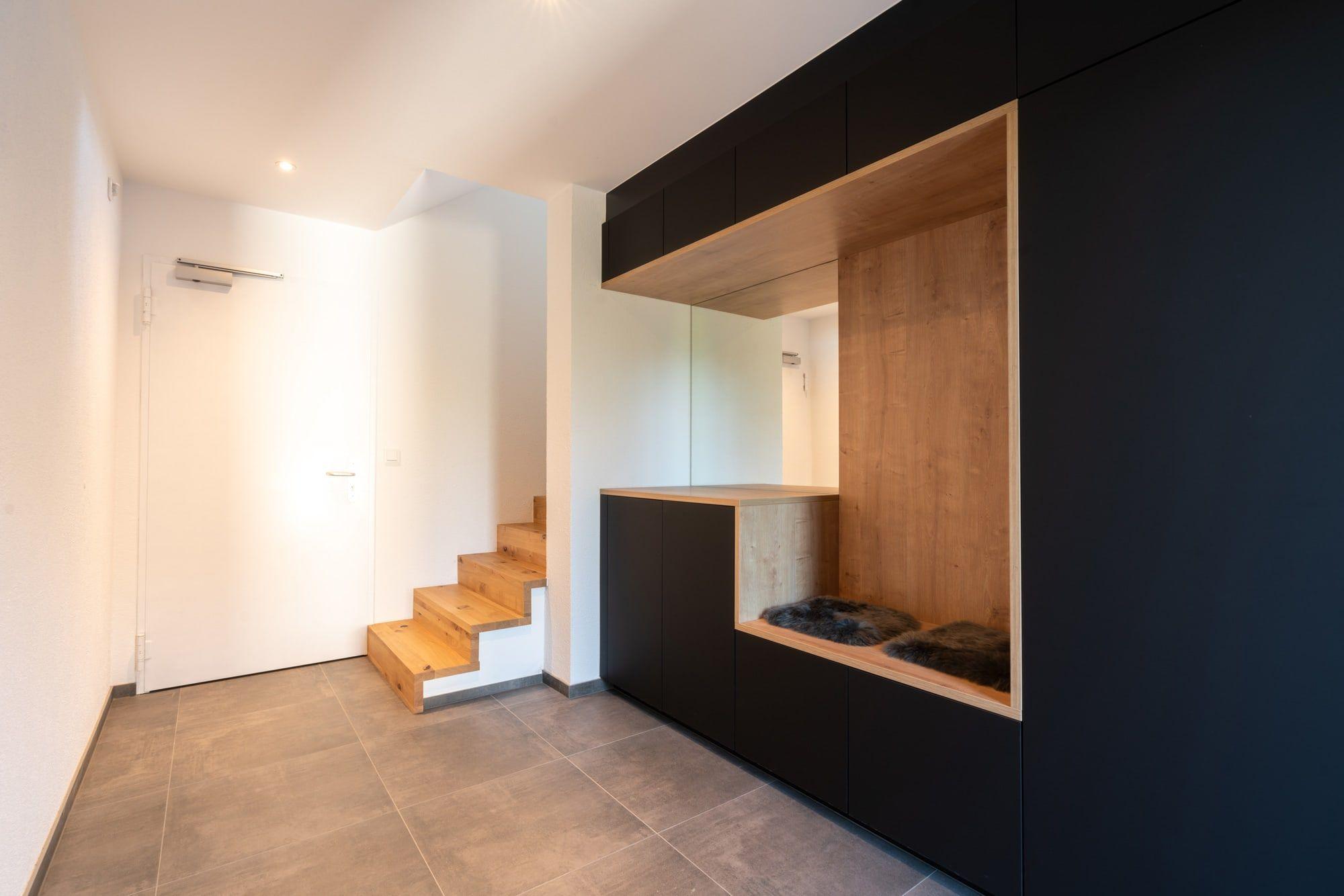 Eingangsflur mit freitragendem Holztreppenaufgang, Einbauschrank mit beleuchteter Holznische und modernem Fliesenboden.