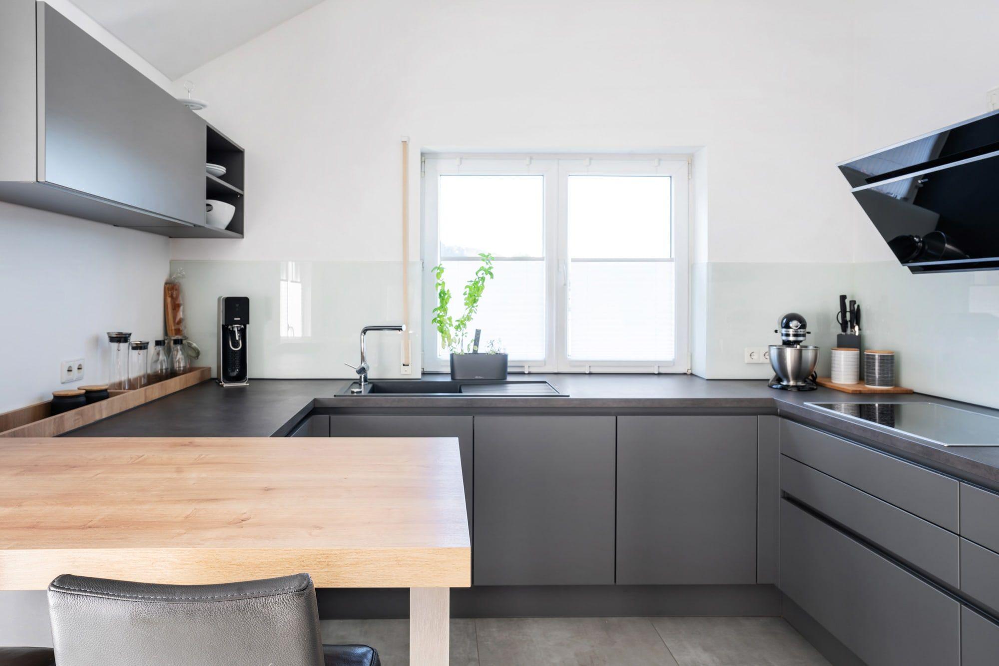 Detailansicht der grauen Küche mit schwarzer Arbeitsplatte, weißer Glasrückwand, Holztheke und modernen Küchengeräten.