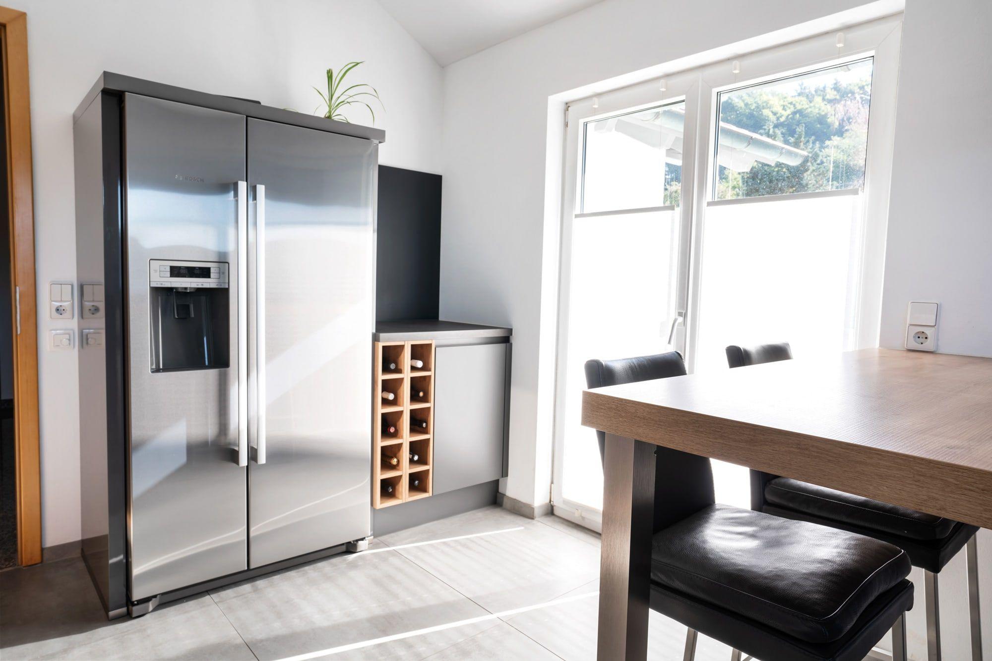 Essbereich mit großem Edelstahl-Side-by-Side-Kühlschrank, Holzweinregal, Holztisch und schwarzen Stühlen.