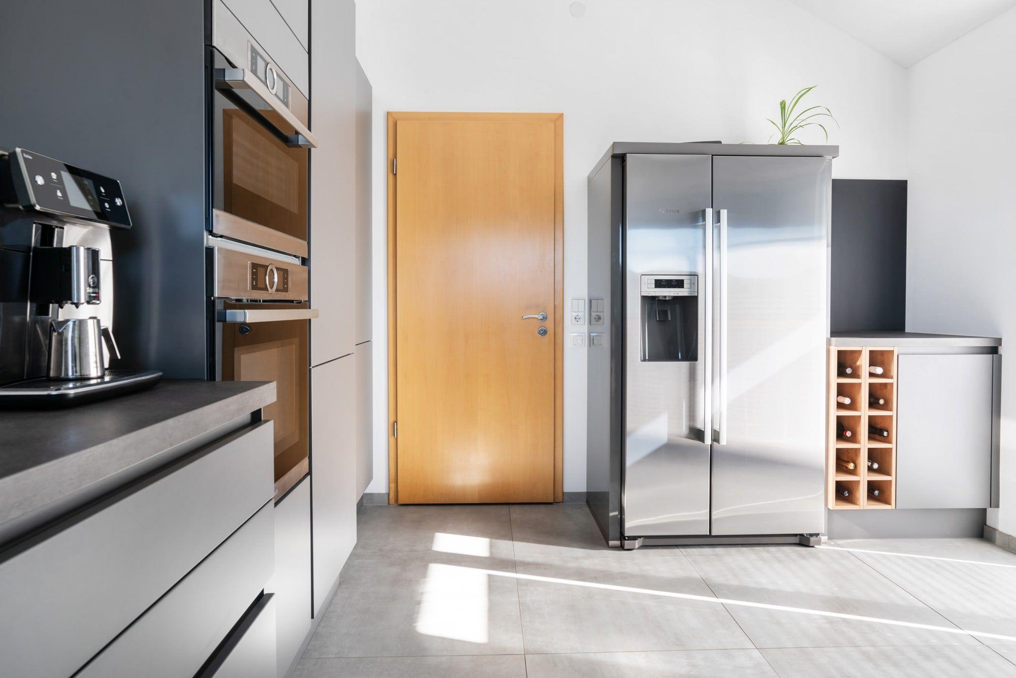 Küche mit eingebauten Edelstahl-Geräten, Side-by-Side-Kühlschrank, Holzweinregal und Holztür als Raumtrenner.