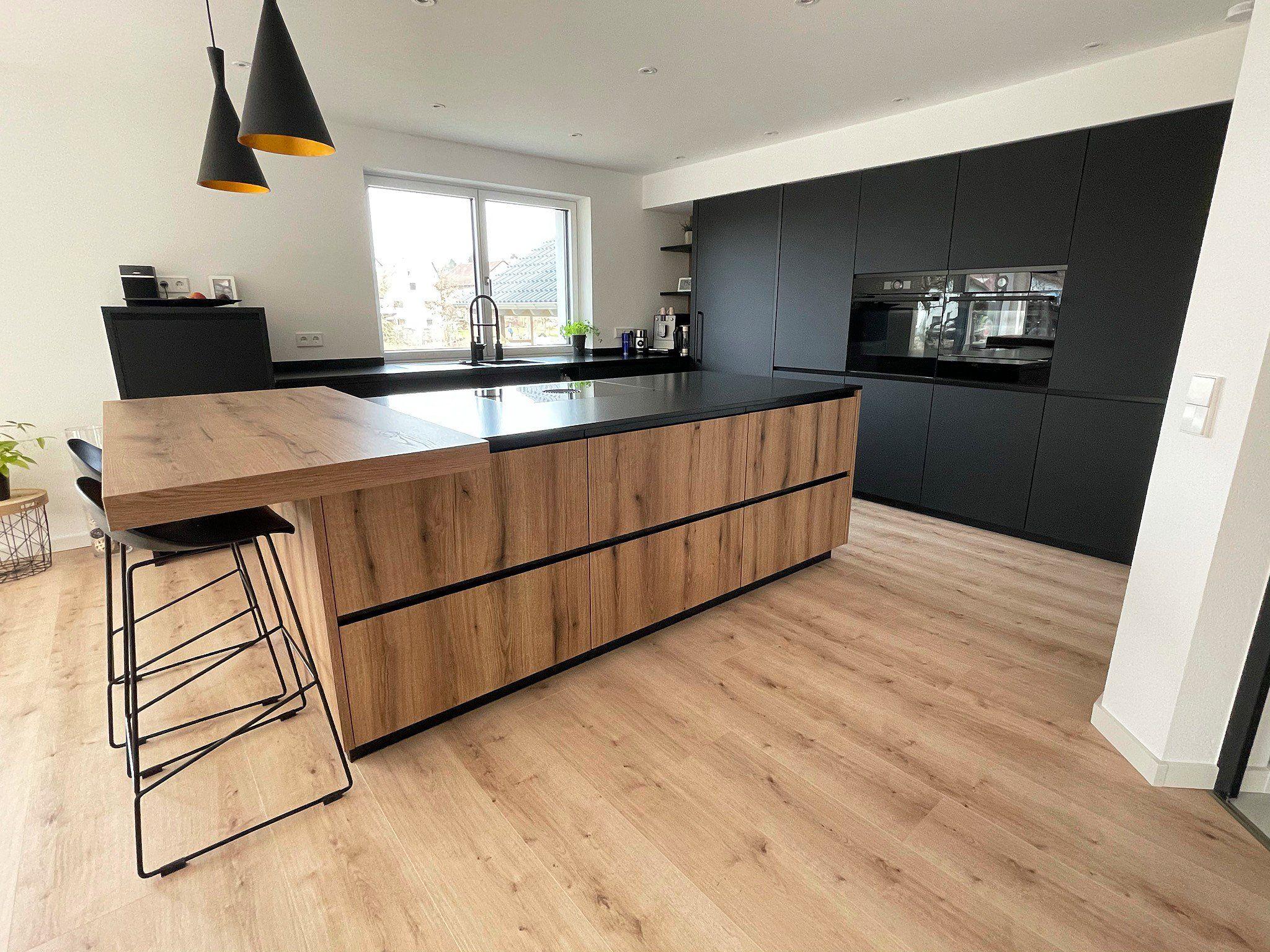 Moderne Küche mit großer Holzkücheninsel, schwarzer Arbeitsplatte, anthrazitfarbenen Hochschränken und Designer-Pendelleuchten.