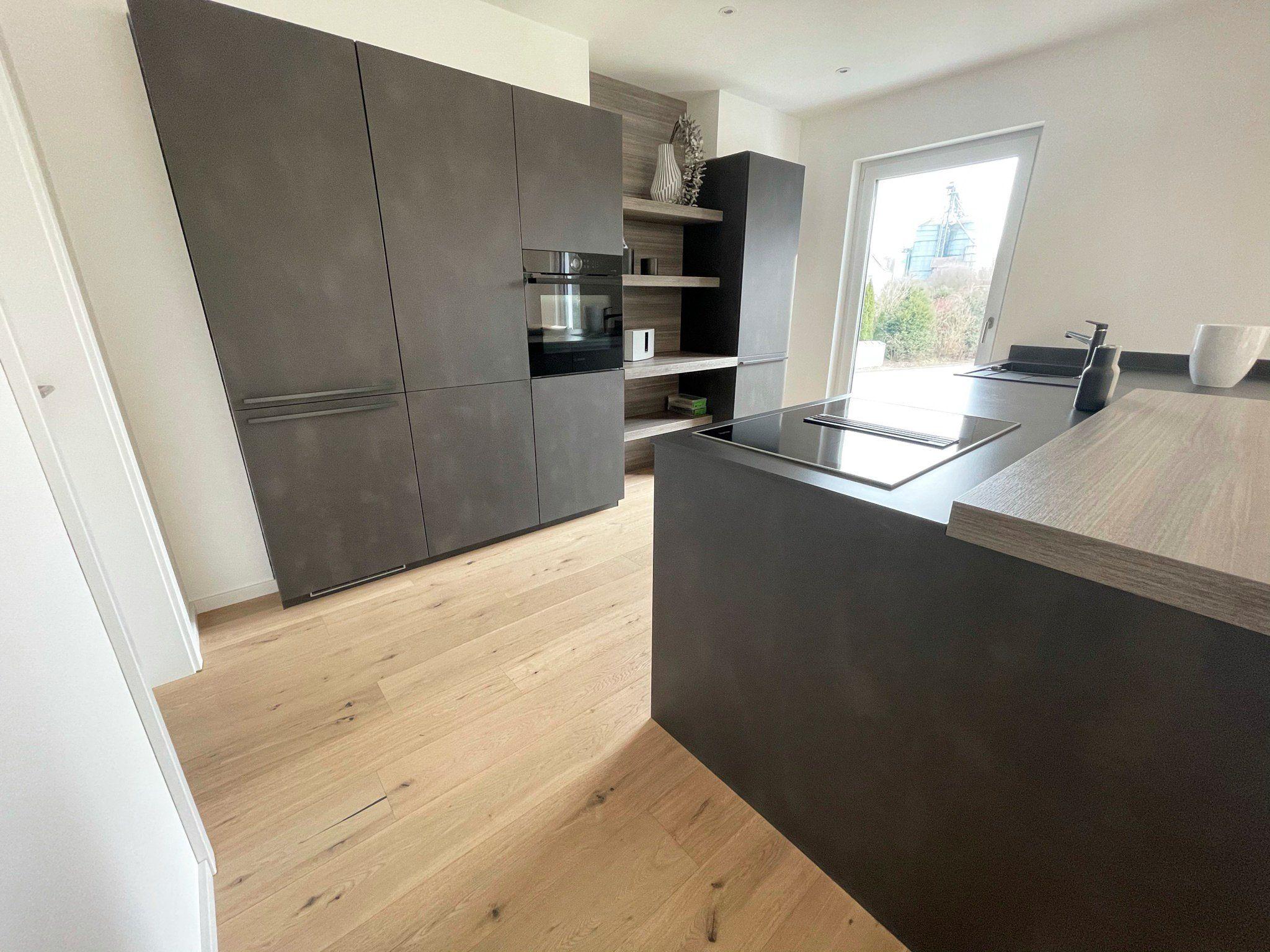 Moderne Küche mit grauen Hochschränken, Kücheninsel mit Kochfeld und Holzoptik-Arbeitsplatte
