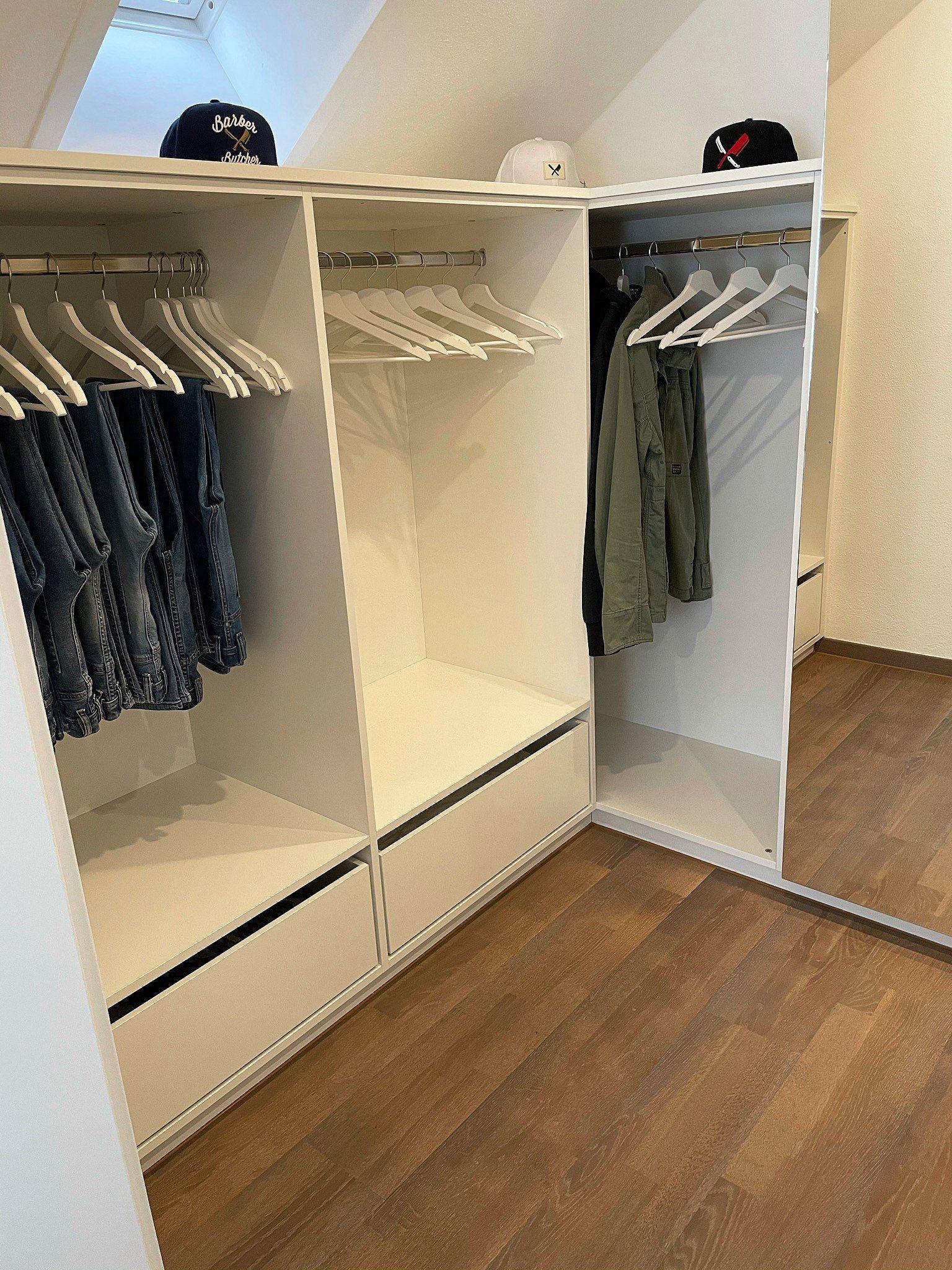 Ankleideraum mit weißen Schrankelementen, hängender Kleidung an Stangen, Baseballkappen auf dem oberen Regalbord und Schubladen.