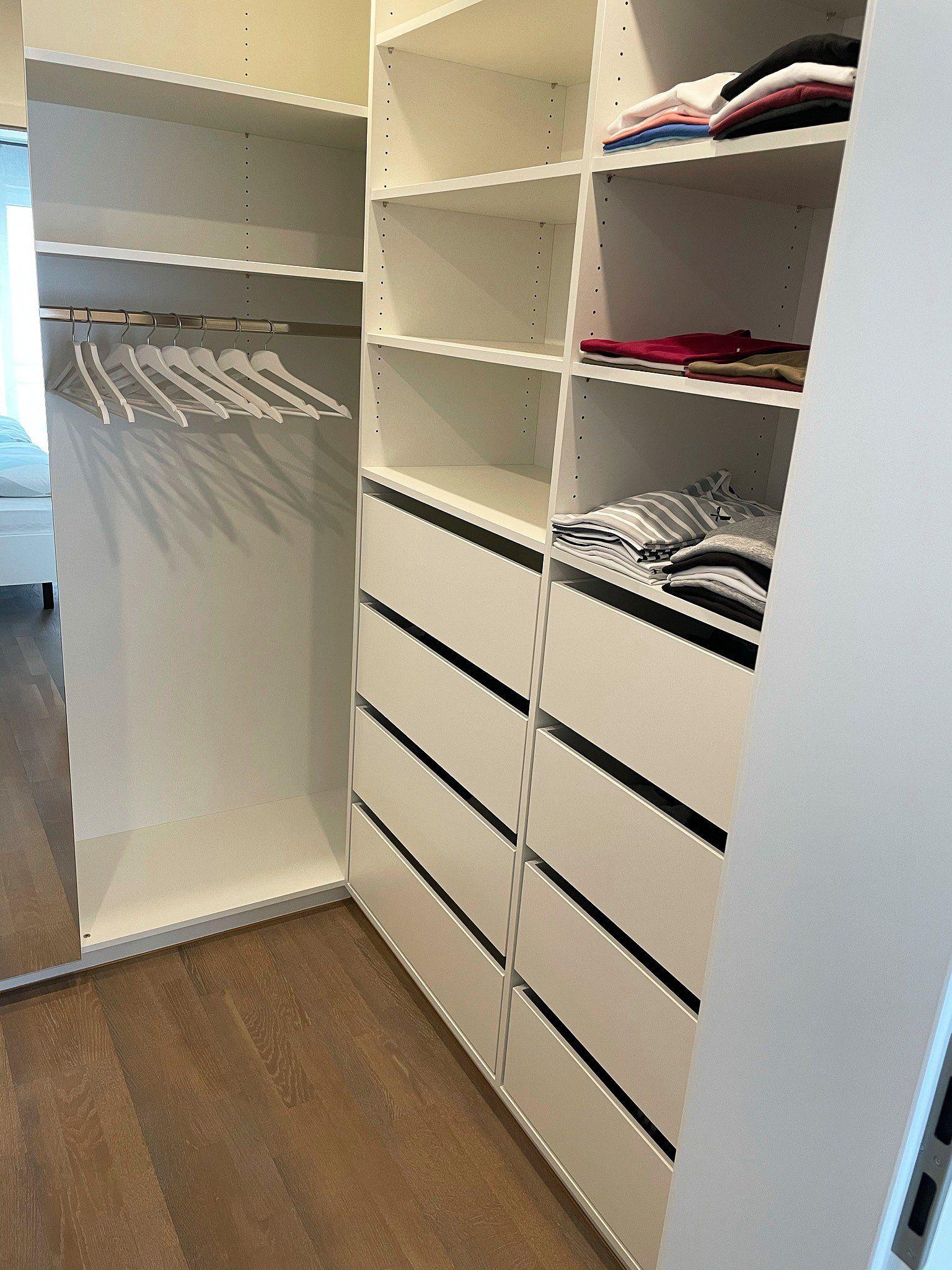 Ankleidezimmer mit hohen weißen Schränken, vielen Schubladen, Kleiderstange und gefalteter Kleidung in offenen Fächern