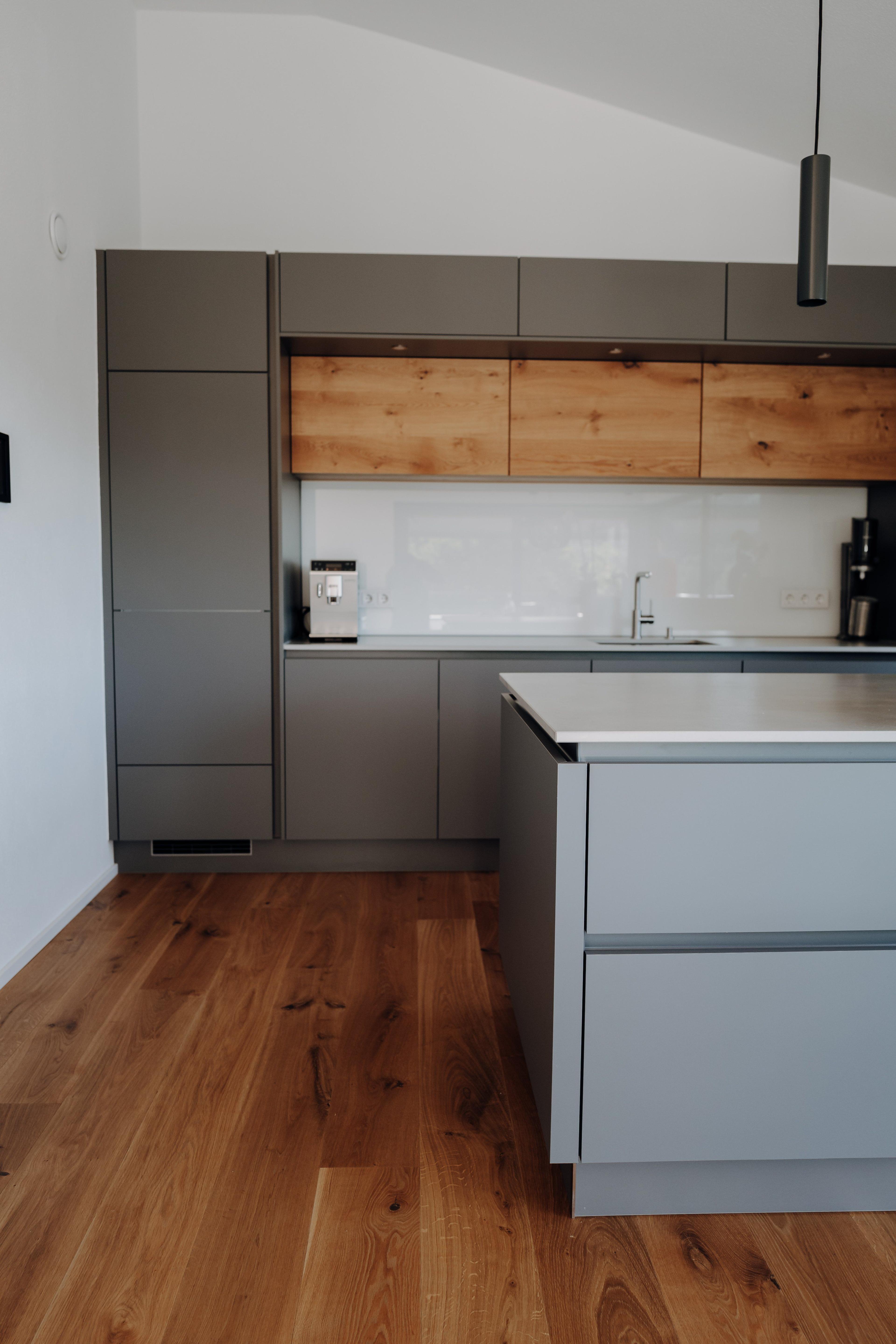 Küche mit L-förmigem Grundriss, anthrazitfarbenen und grauen Fronten, Holzelementen und offener Raumgestaltung