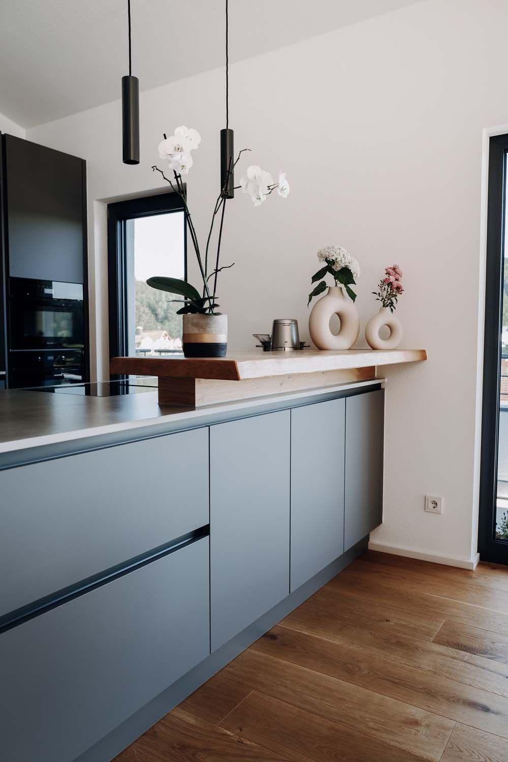 Küchentheke mit grauer Front, Holzaufsatz, weißen Deko-Vasen, Orchideen und schwarzen Pendelleuchten.