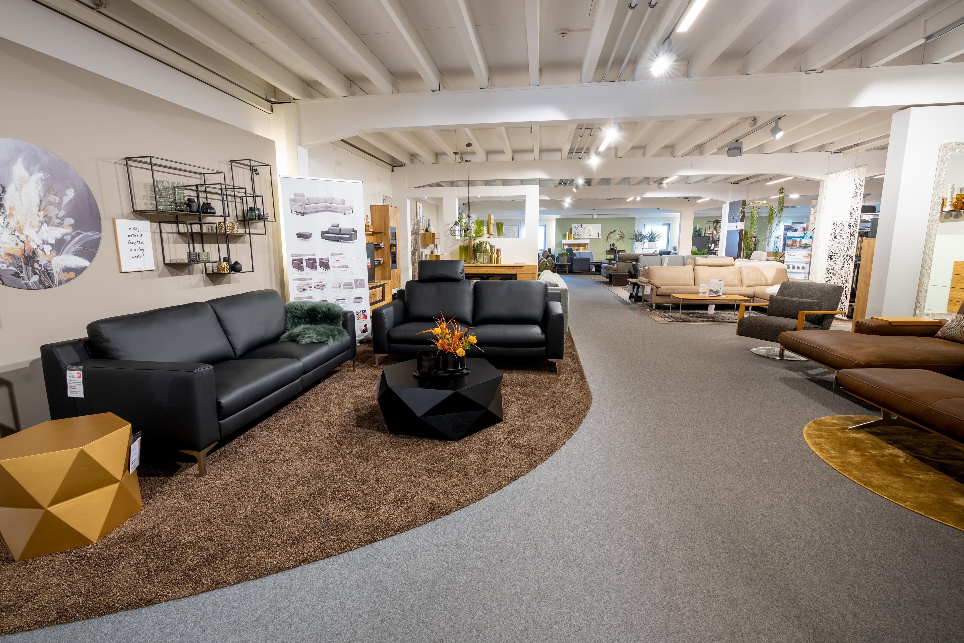 Möbelhaus-Showroom mit schwarzen Ledersofas, modernen Couchtischen und verschiedenen Wohnzimmermöbeln in großer Ausstellungshalle.