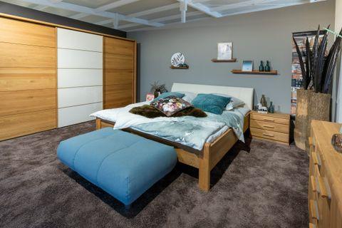 Modernes Schlafzimmer mit Holzbett, blauer Bettbank, großem Kleiderschrank und grauer Wand mit Wandregalen.