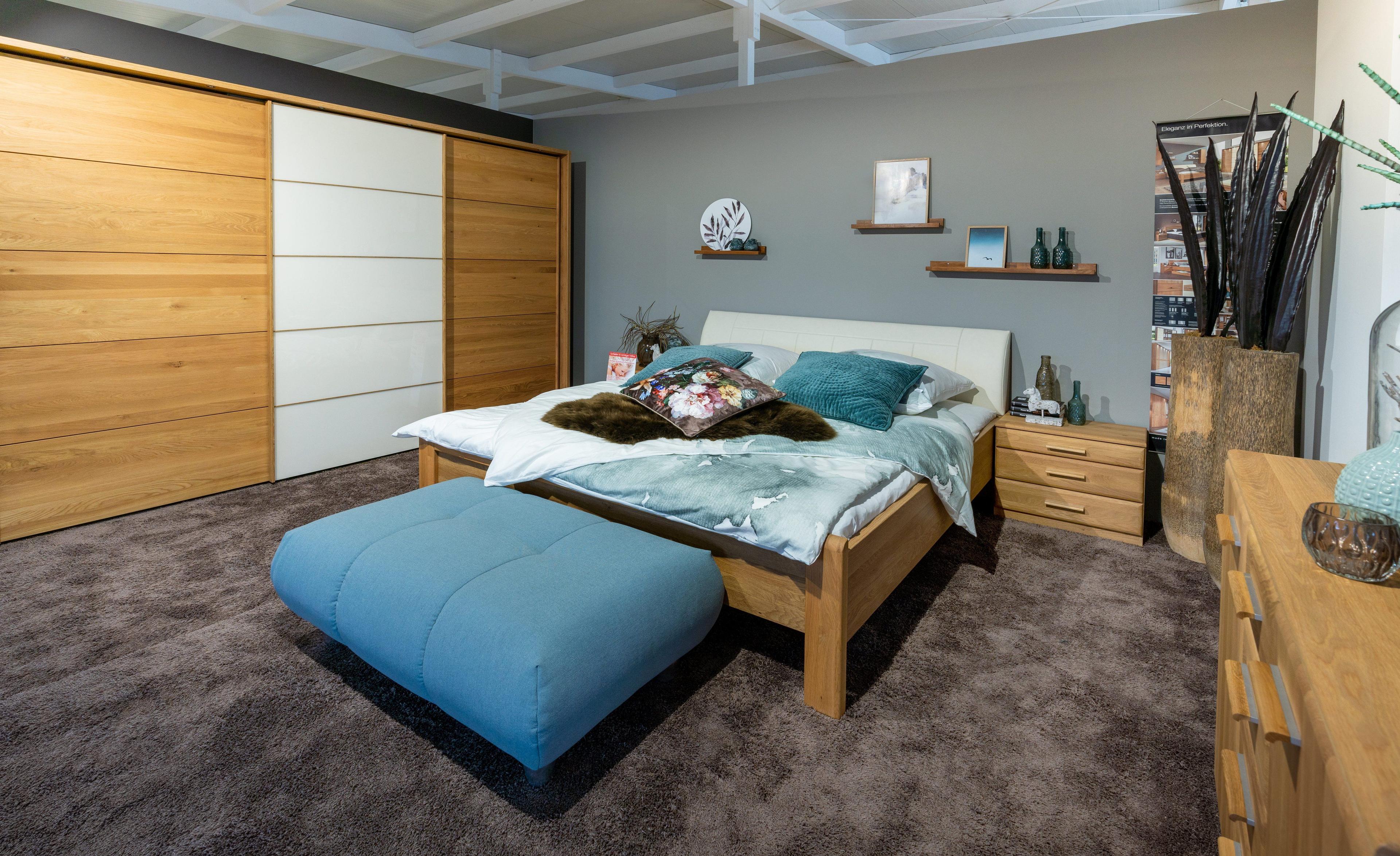 Modernes Schlafzimmer mit Holzbett, blauer Bettbank, großem Kleiderschrank und grauer Wand mit Wandregalen.