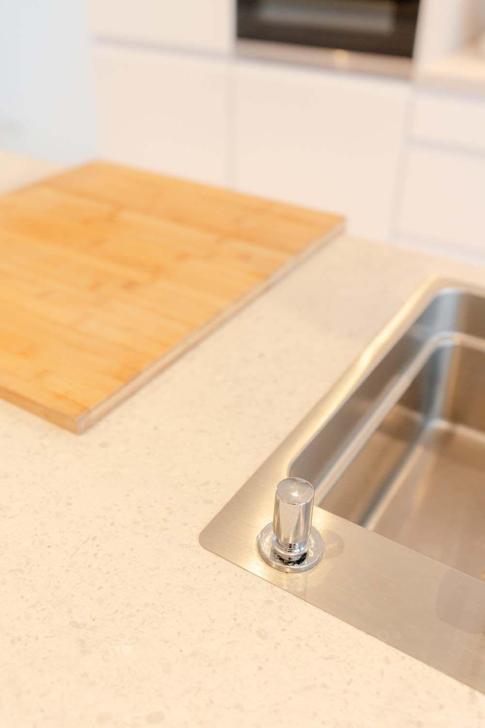 Detailansicht der Spüle mit Seifenspender und Holzschneidebrett auf heller Arbeitsplatte.