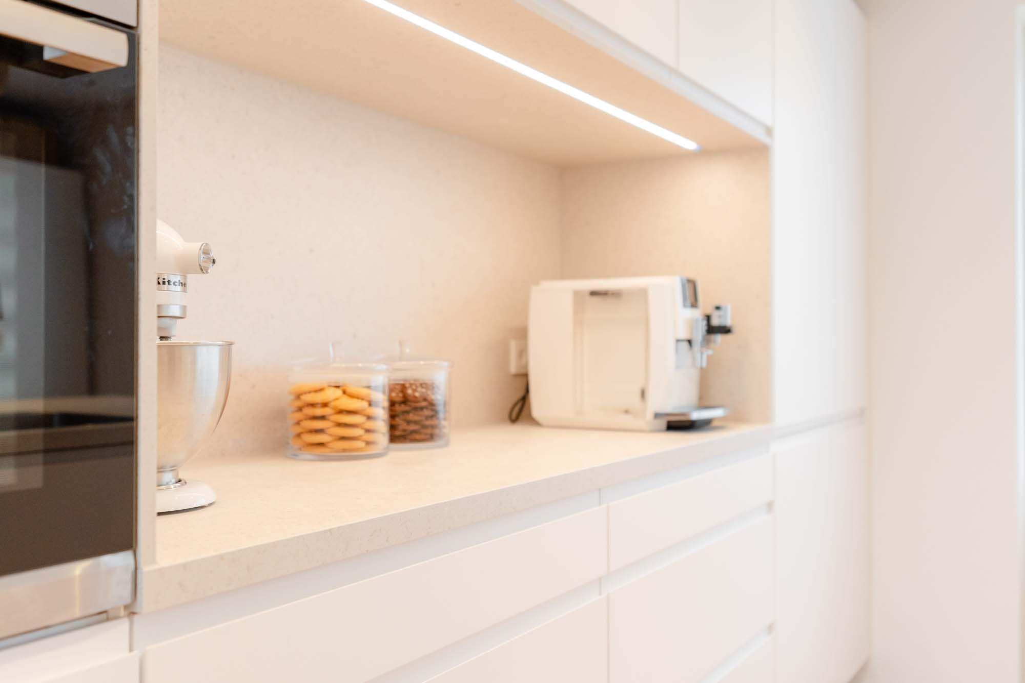 Beleuchtete Arbeitsnische mit Küchenmaschine, Kaffeevollautomat und Vorratsgläsern mit Keksen.