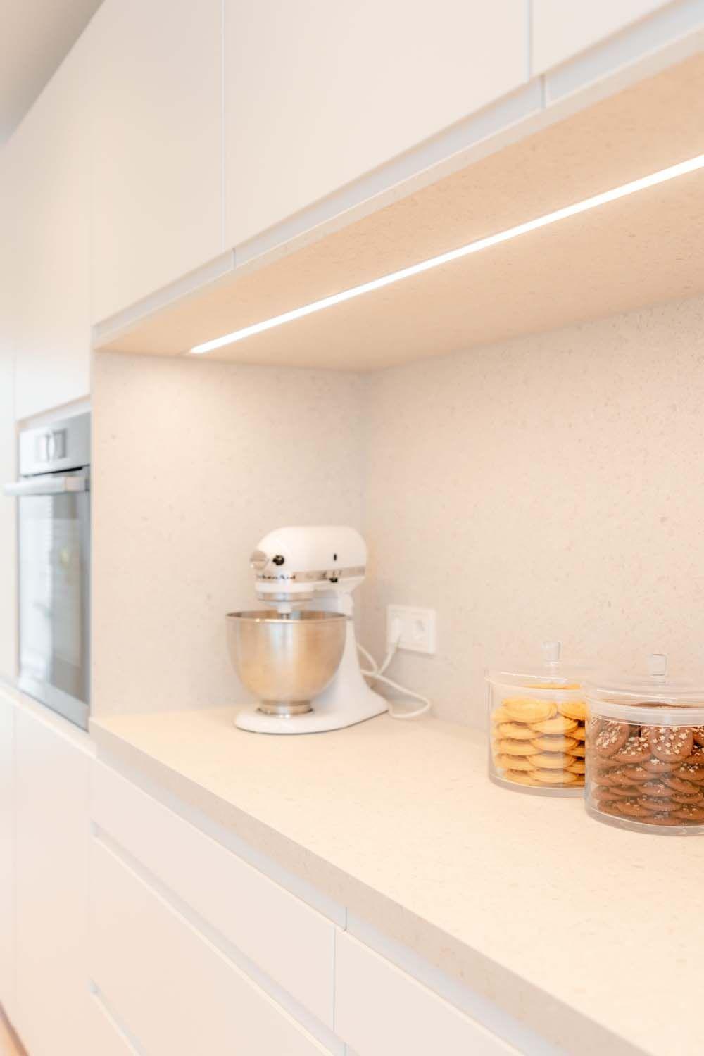 Beleuchtete Küchennische mit weißer KitchenAid-Küchenmaschine und Vorratsgläsern unter LED-Beleuchtung.