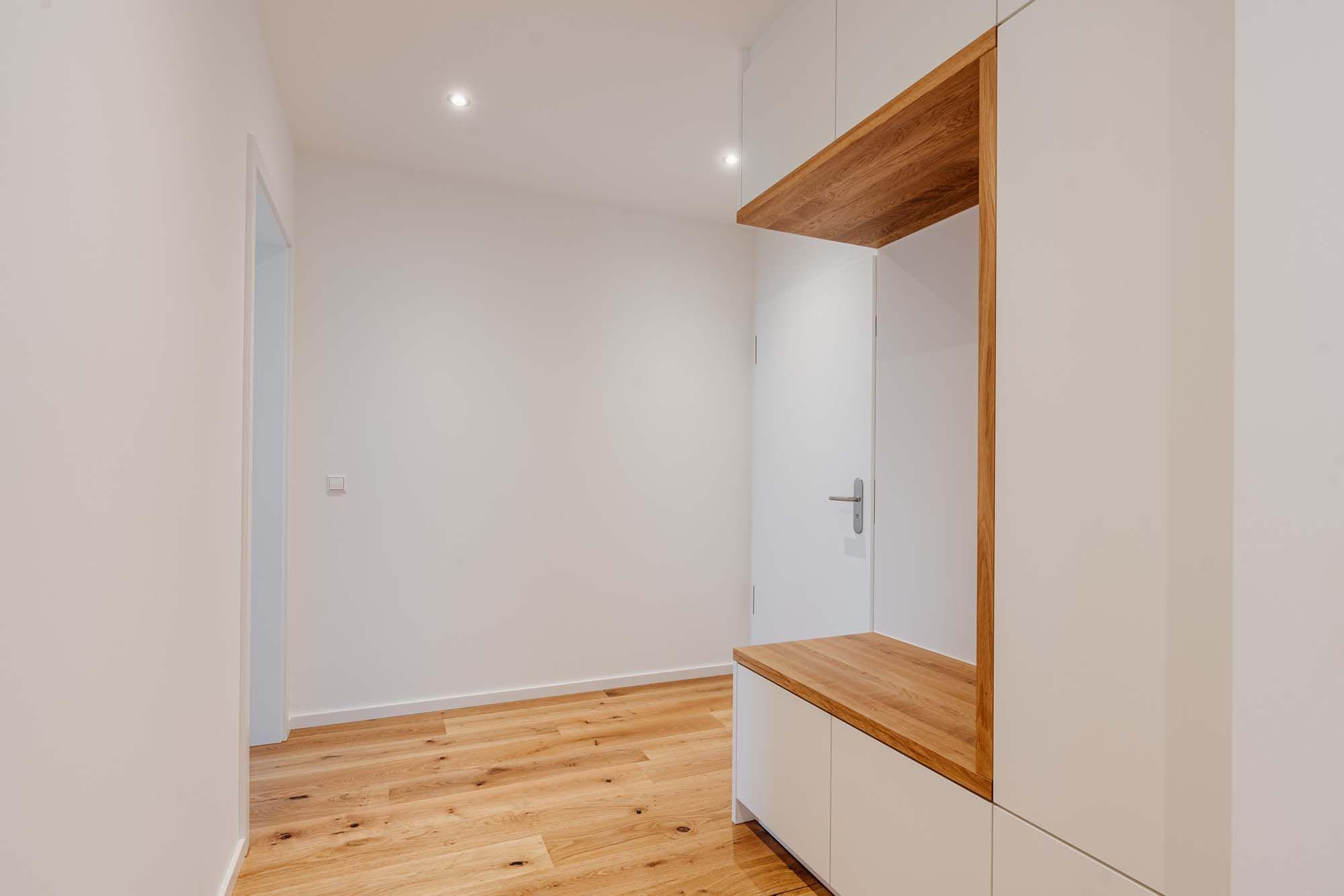 Moderner Flur mit Einbauschrank, Eichennische als Sitzgelegenheit und weißen Türen auf Holzparkett.