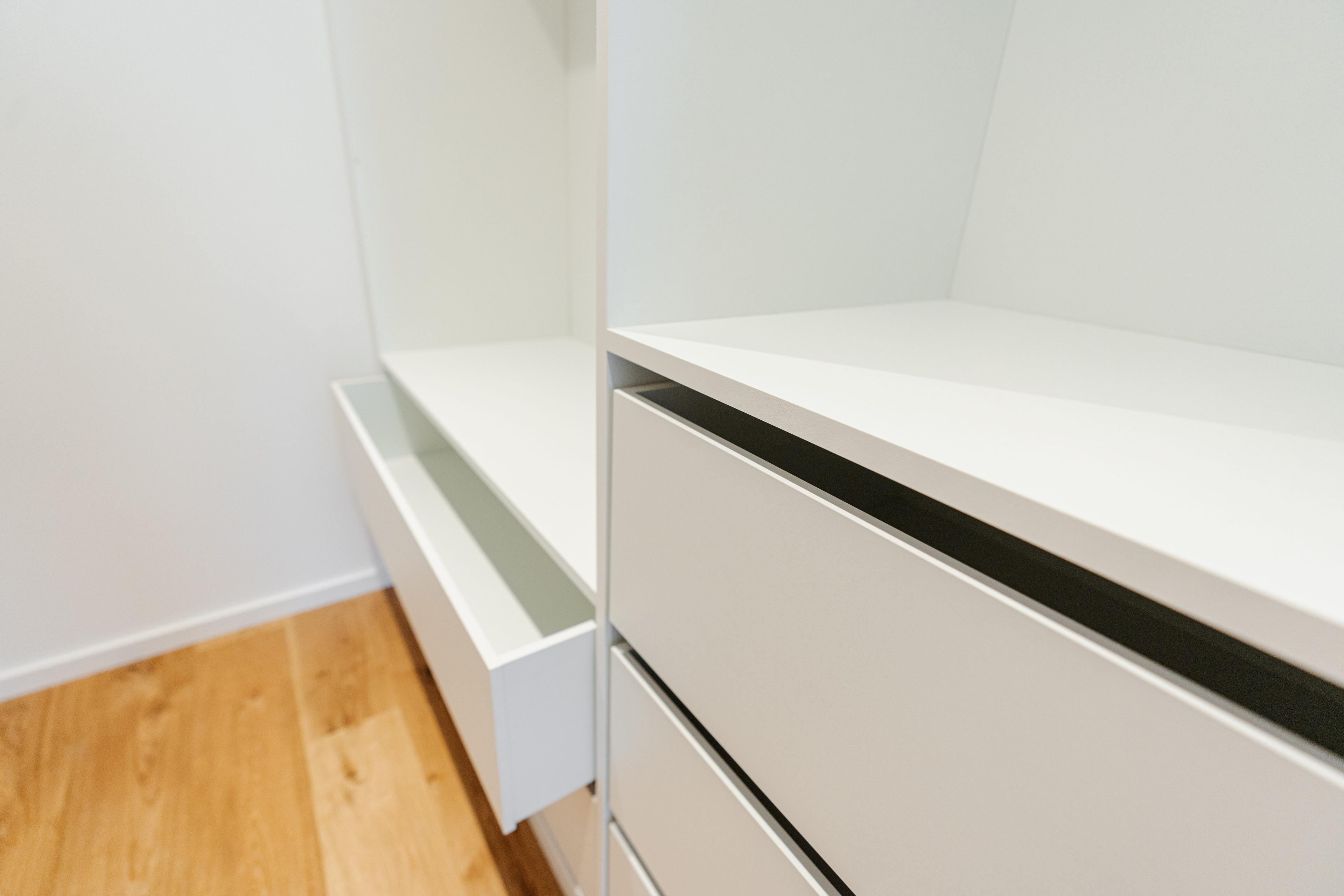 Geöffnete weiße Schrankschubladen mit Vollauszug zeigen Innenausstattung auf Holzparkett in modernem Ankleidezimmer.