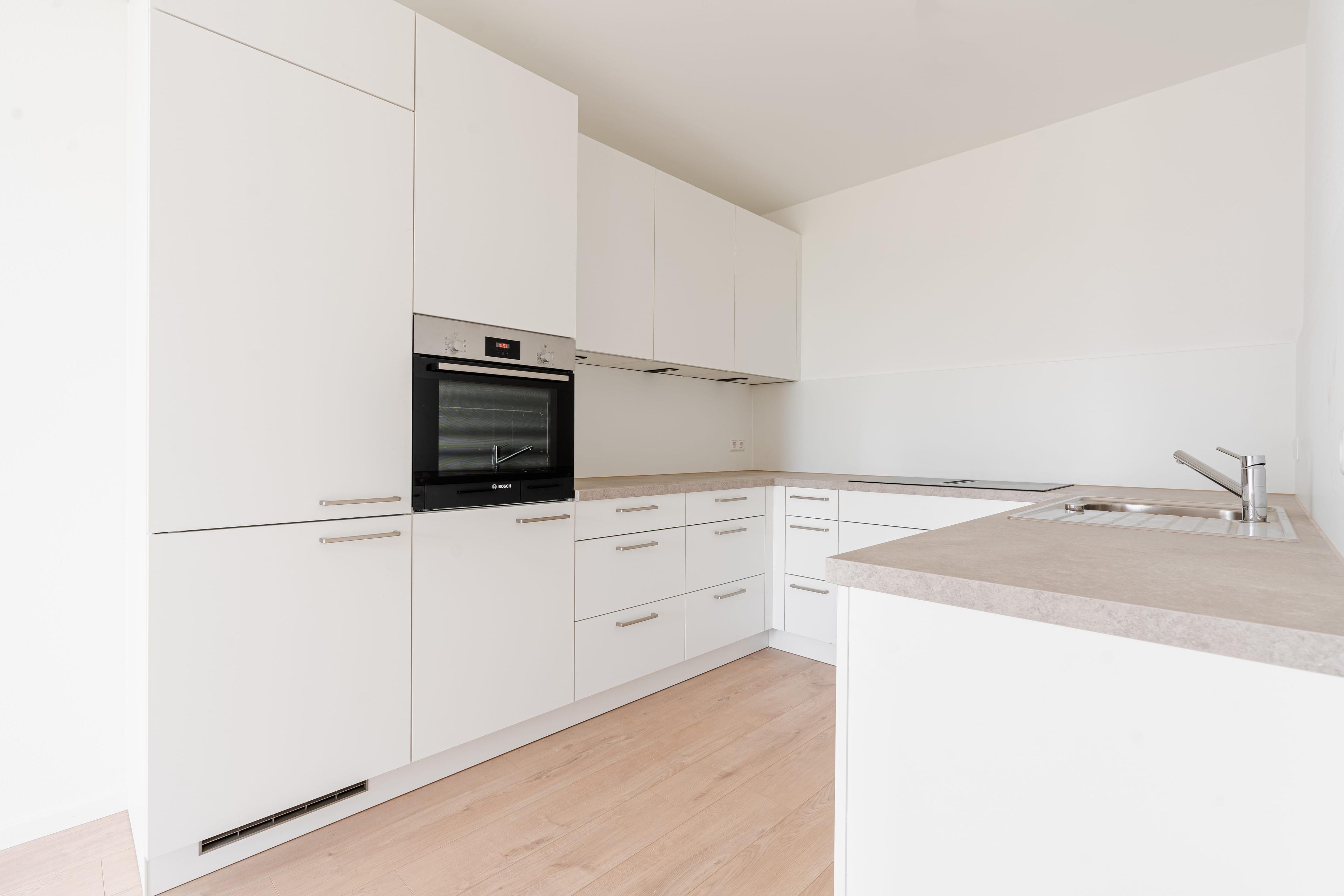 Eckküche in Weiß mit beiger Arbeitsplatte, eingebautem Backofen, Dunstabzug und modernen Edelstahlgriffen.