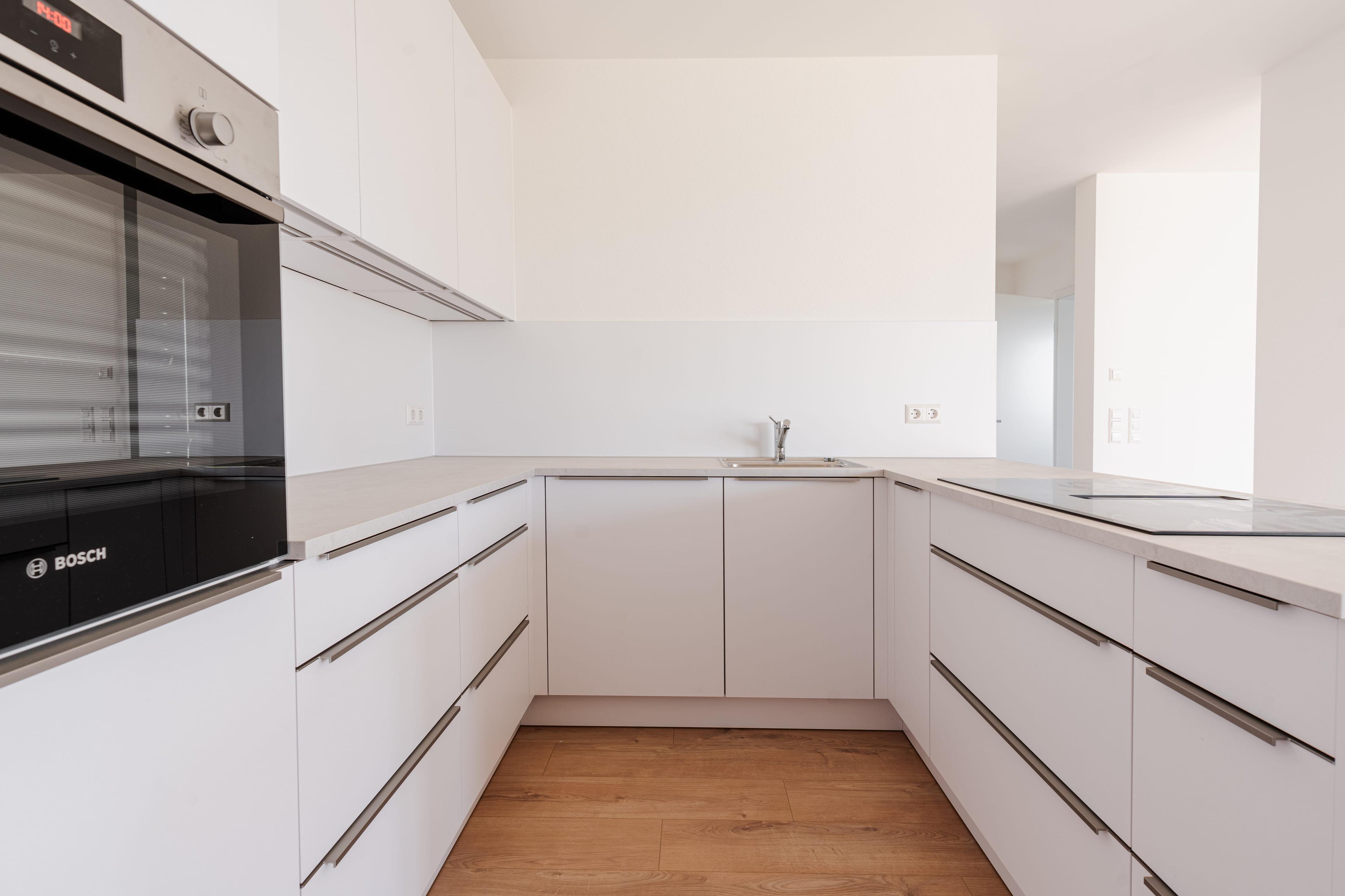 U-förmige Küche mit weißen Unterschränken, Bosch-Backofen und heller Arbeitsplatte auf Holzboden.