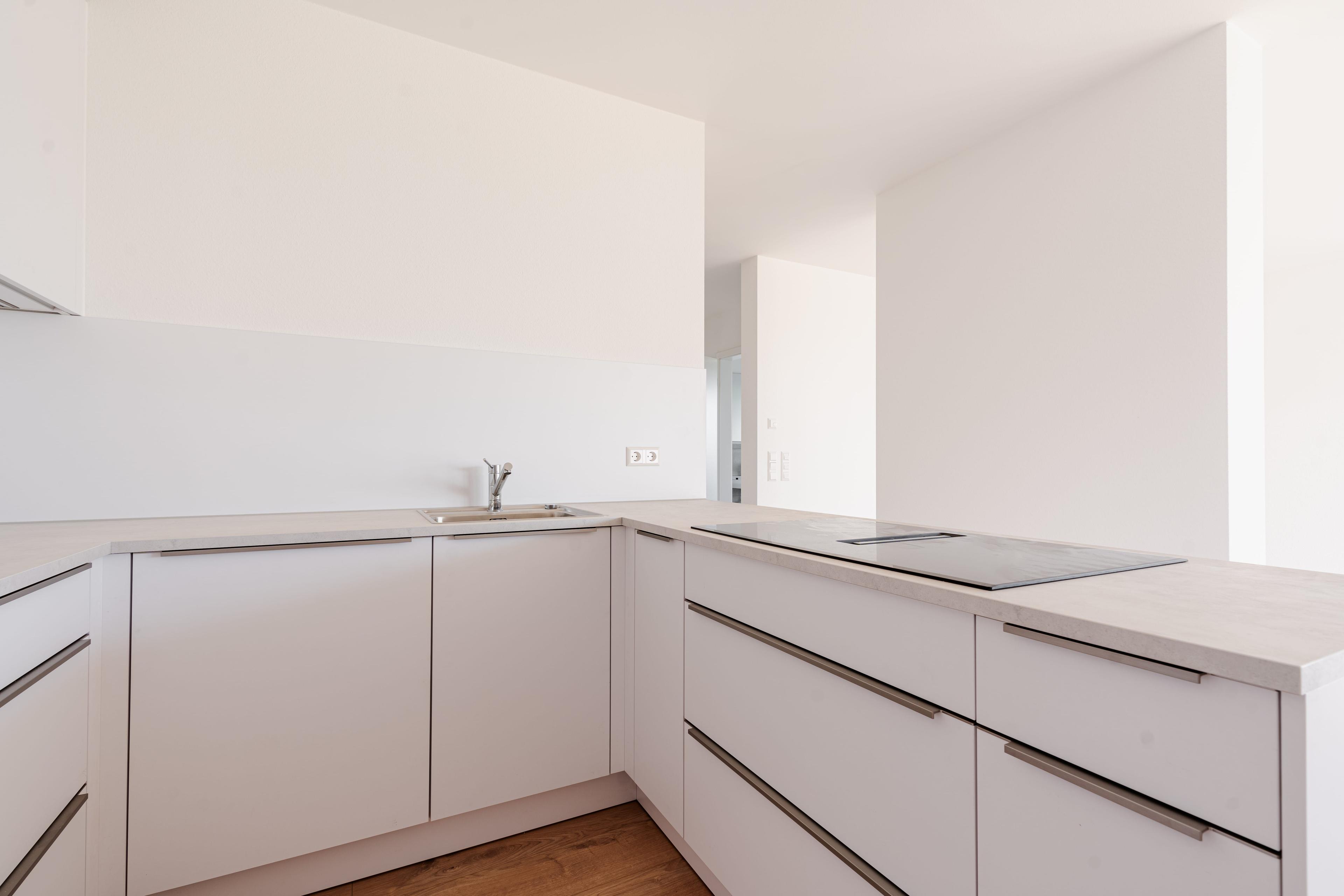 Eckküche mit weißen grifflosen Fronten, integriertem Kochfeld und minimalistischem Design.
