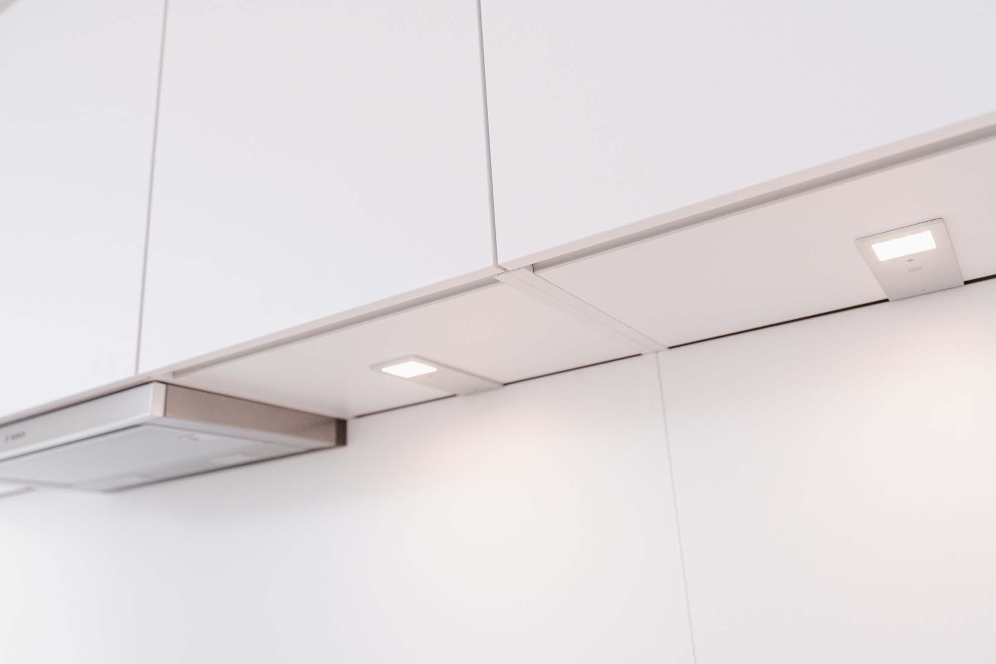 Nahaufnahme der LED-Unterbauleuchten unter weißen Oberschränken mit warmweißem Licht.