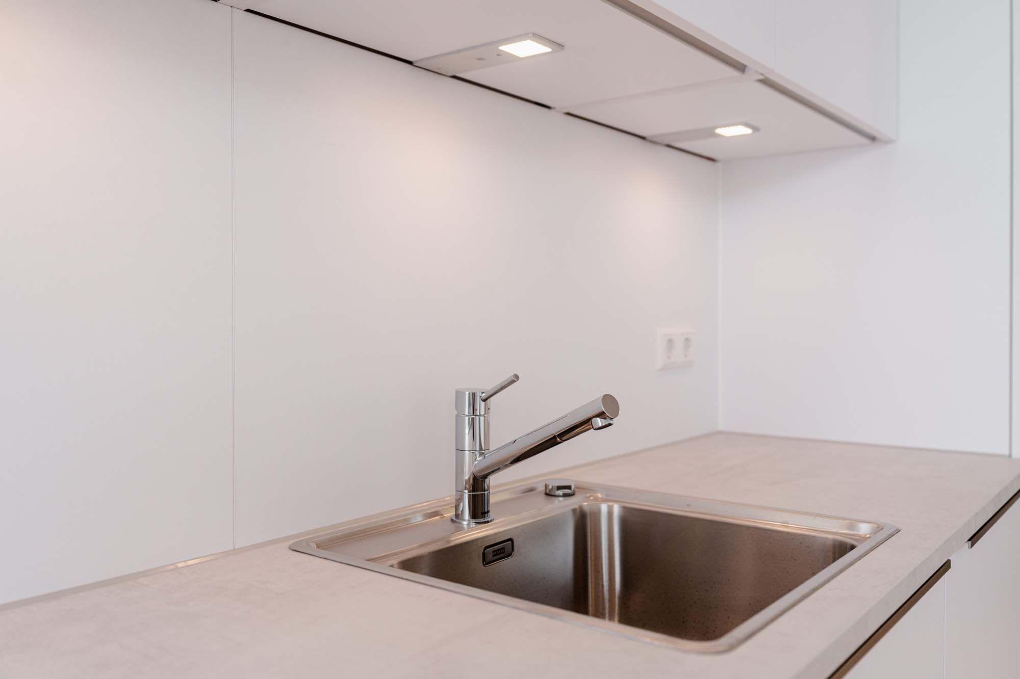 Spülbereich mit Edelstahlspüle, modernem Wasserhahn und LED-Unterbauleuchten.