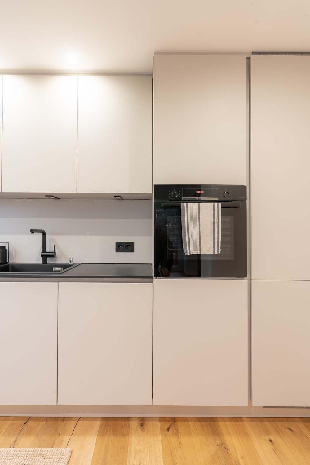 Detailansicht der Küchenzeile mit eingebautem Backofen, beigen Fronten und schwarzen Arbeitsplatten.