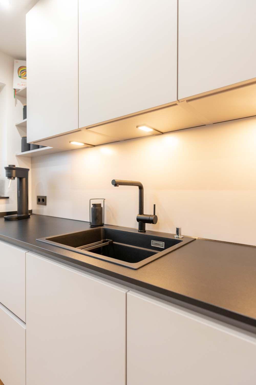 Spülbereich mit LED-Unterbauleuchten, schwarzer Armatur und schwarzer Spüle in dunkler Arbeitsplatte.