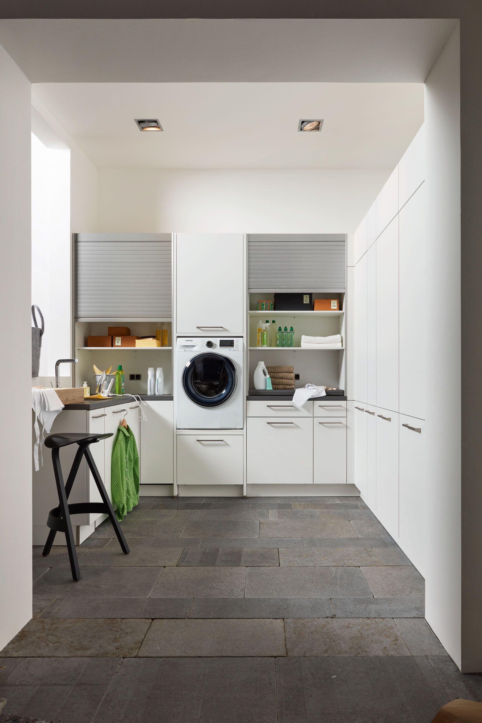 Heller Hauswirtschaftsraum in Weiß mit Rolljalousie-Schränken, integrierter Waschmaschine, Arbeitsplatz und stilvoller Deckenbeleuchtung.