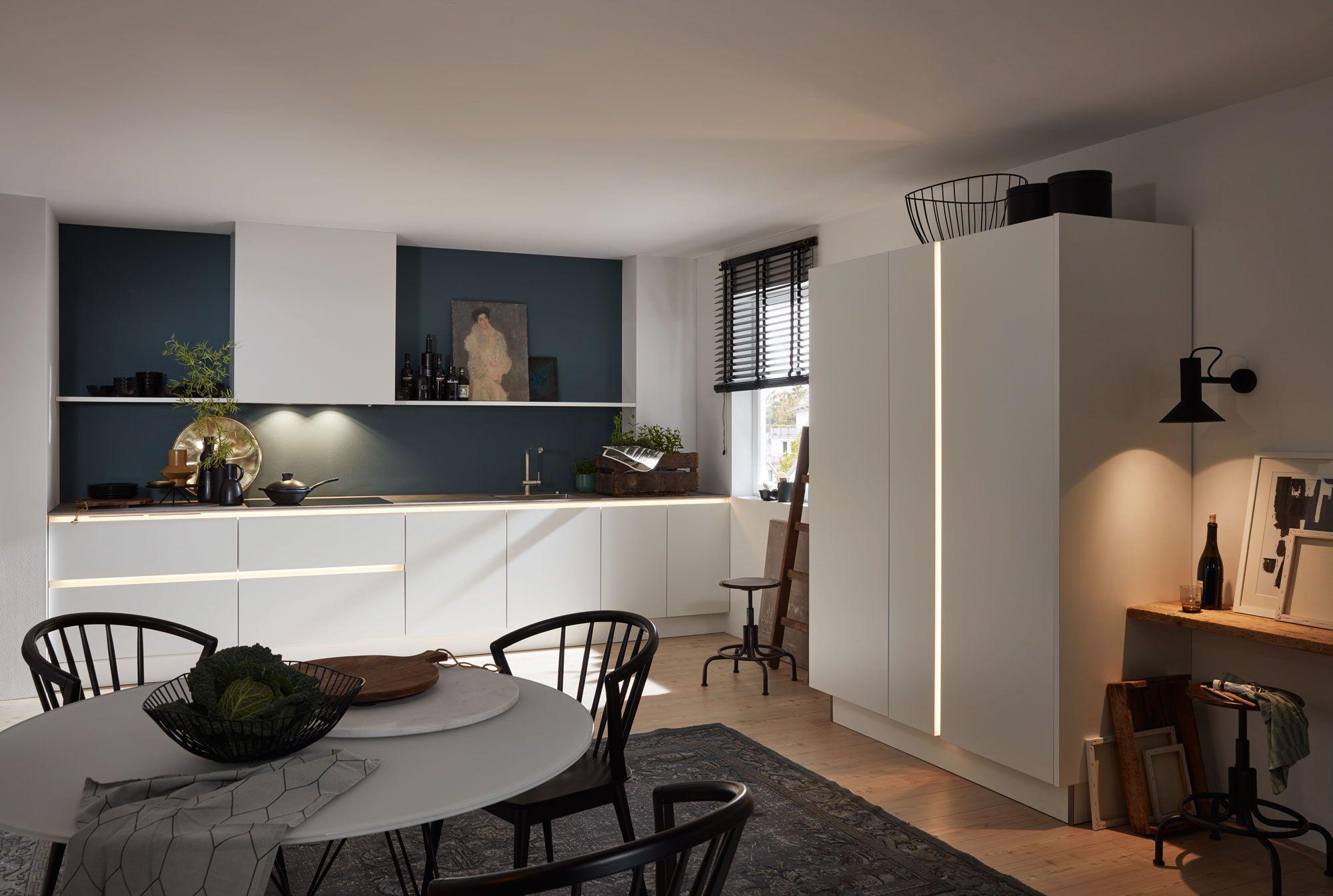 Moderne Küche in Weiß mit petrolblauer Nischenwand, LED-Beleuchtung und integriertem Hochschrank mit stilvoller Griffleiste.