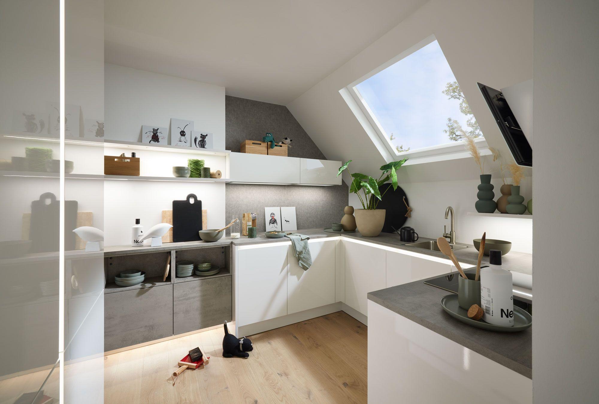 Moderne L-Küche mit hellen, glänzenden Fronten, natürlichen Dekoelementen und einer großen Dachfensteröffnung.