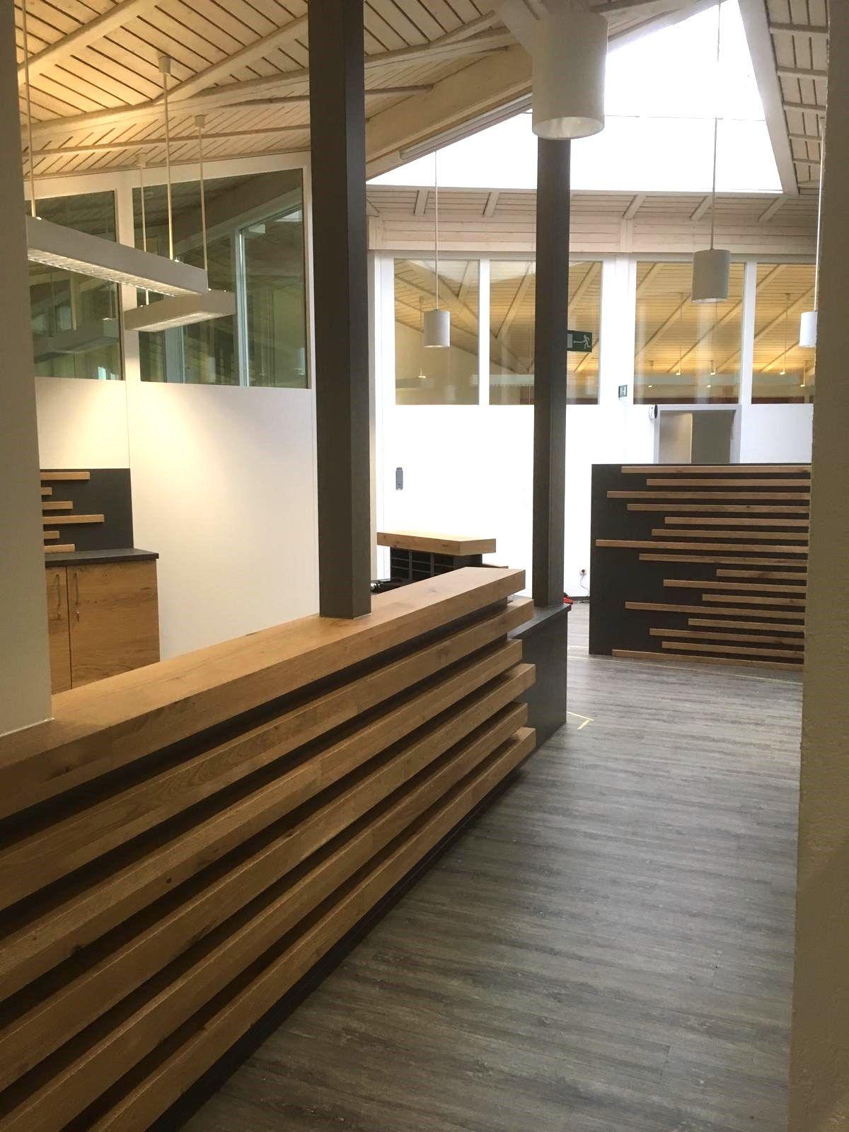 Moderner Showroom einer Schreinerei mit Holzlamellen-Empfangstresen, sichtbarer Holzbalken-Dachkonstruktion und Glasgalerie im Obergeschoss.