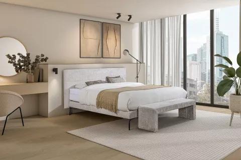 Modern eingerichtetes Schlafzimmer mit Polsterbett, weicher Tagesdecke, Sitzbank und Schminktisch – lichtdurchflutet mit Blick auf die Skyline.