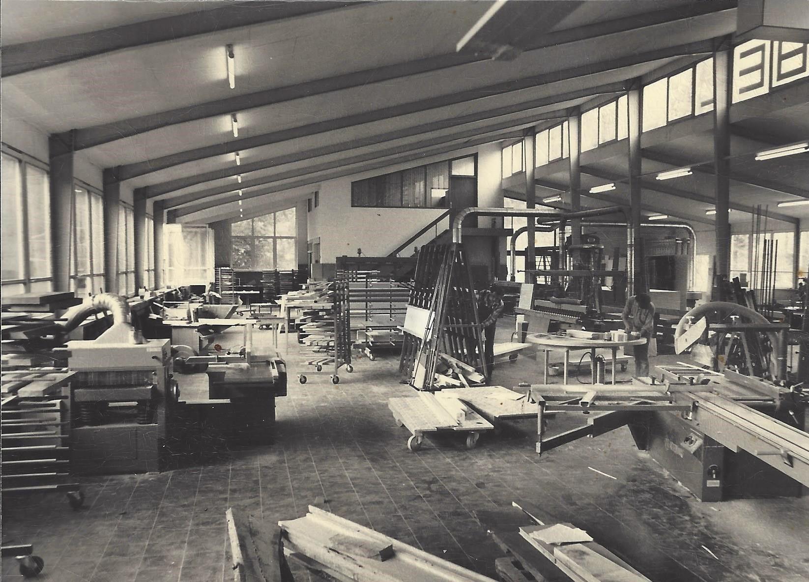 Historische Schwarz-Weiß-Aufnahme einer Holzwerkstatt mit Balkendecke, Werkbänken, Holzlagerung und traditionellen Tischlereimaschinen aus den 1950er/60er