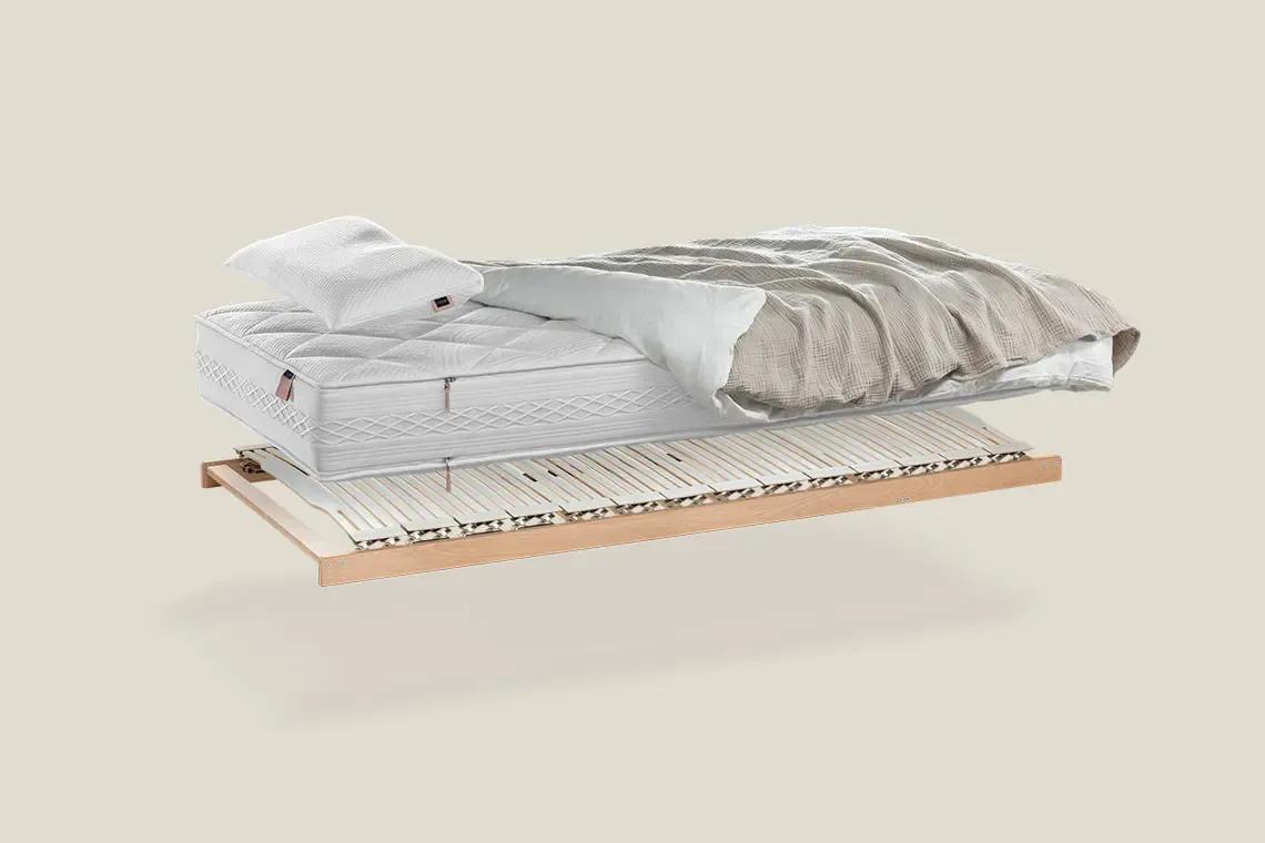 Querschnitt eines Betts mit verstellbarem Lattenrost aus Holz, darauf eine weiße Matratze mit Kissen und beigem Bettzeug.