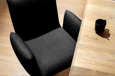 Moderner Esszimmerstuhl mit gepolstertem, anthrazitfarbenem Stoffbezug und Holzbeinen – platziert an einem massiven Esstisch aus Eiche.