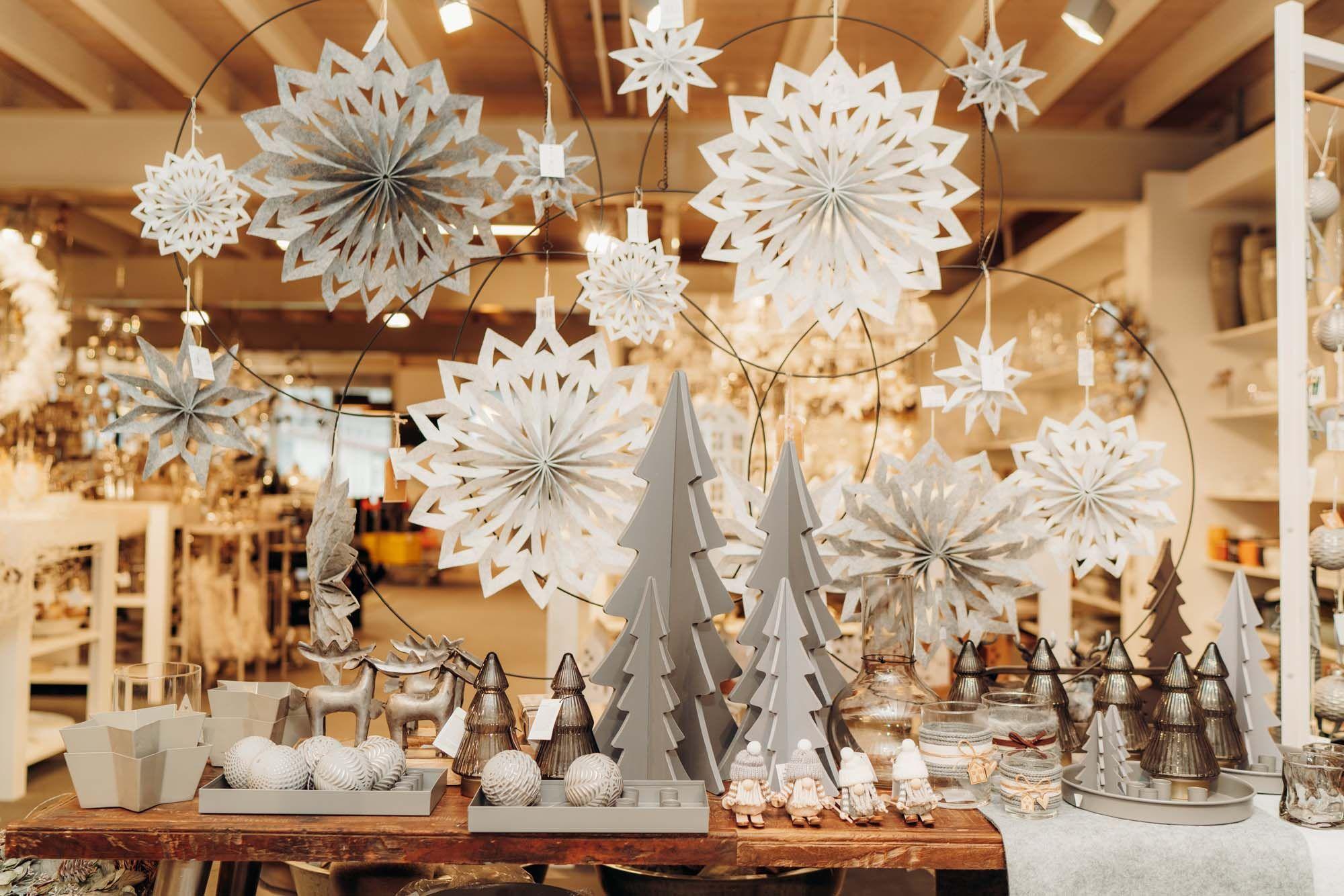 Festliche Weihnachtsdeko mit weißen Papiersternen, Holztannenbäumen und Christbaumkugeln in der Boutique von Möbel Grell.