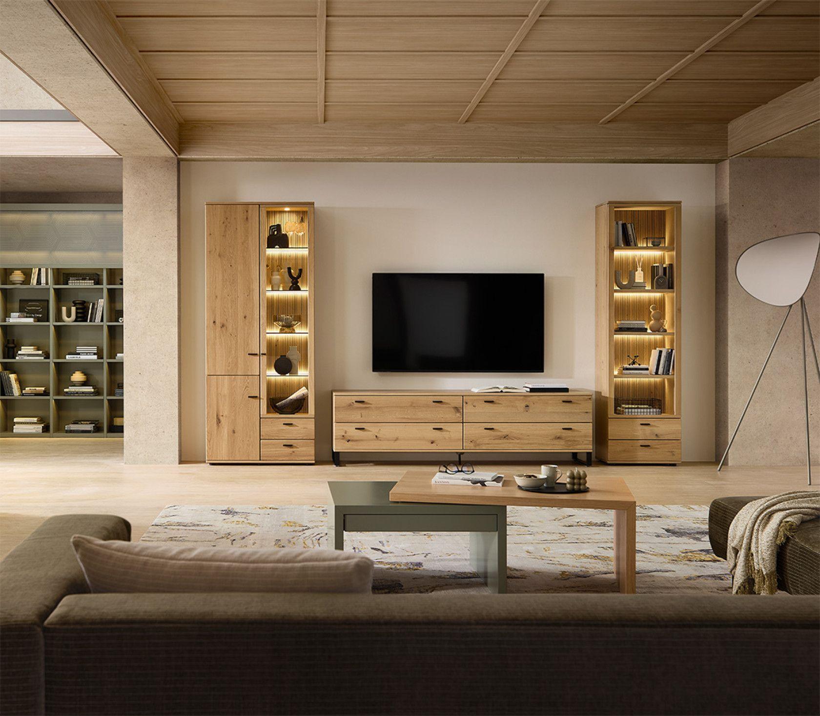  Modernes Wohnzimmer mit natürlicher Holzdecke, beigen Sofas, TV-Wand aus Holz mit beleuchteten Vitrinen, grünem Bücherregal links und weißer Stehleuchte auf gemustertem Teppich.