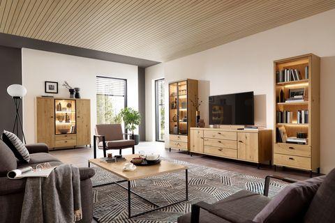 Gemütlich eingerichtetes Wohnzimmer mit Wohnwand, Vitrinen, Bücherregal und Couchtisch in Asteiche – kombiniert mit dunklen Polstermöbeln und modernem Dekor.