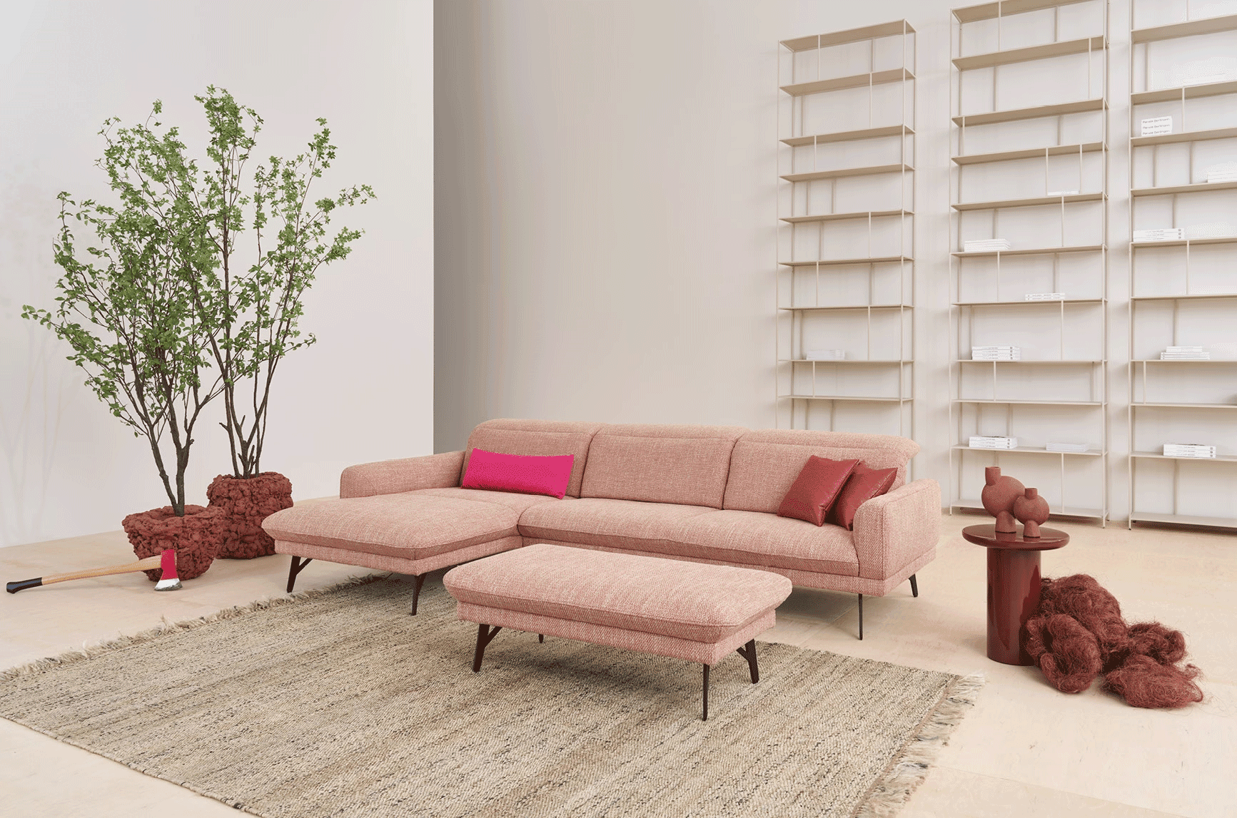 Rosafarbenes Ecksofa mit Hocker vor minimalistischem Wandregalsystem aus Holz, dekoriert mit großer Zimmerpflanze und roten Akzenten.