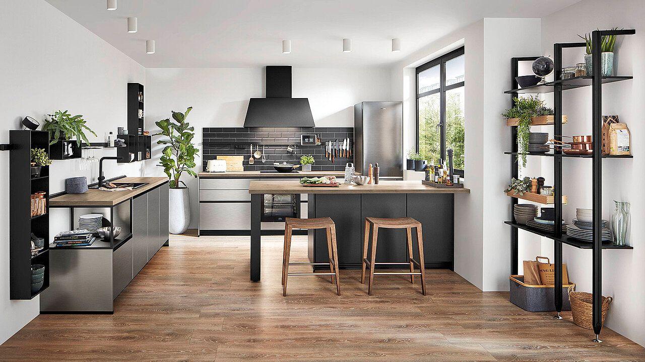 Moderne Kücheninsel in Anthrazit mit Holzarbeitsplatte, zwei Holzbarhockern, schwarzer Fliesenrückwand und offenen Metallregalen in einer hellen Küche mit Holzboden.