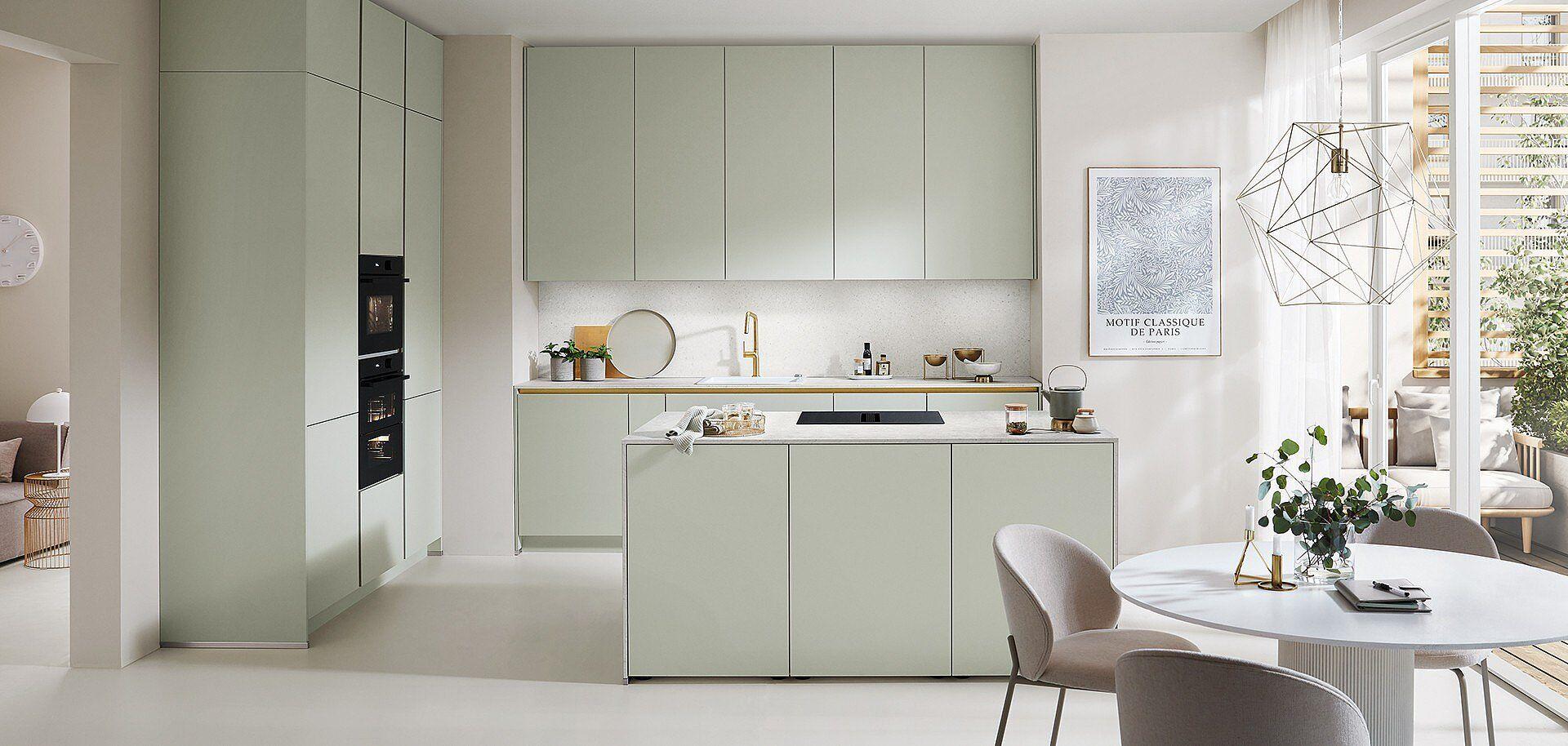 Moderne Kücheninsel in Salbeigrün mit weißer Marmorarbeitsplatte, integriertem Kochfeld und elegantem Essbereich in einem hellen, offenen Wohnraum.