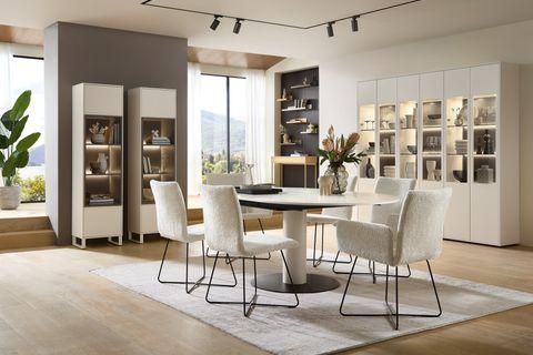 Modernes Esszimmer mit rundem Esstisch, weißen Stühlen mit Bouclé-Bezug, stilvollen Vitrinen und eleganter Dekoration in lichtdurchflutetem Raum.