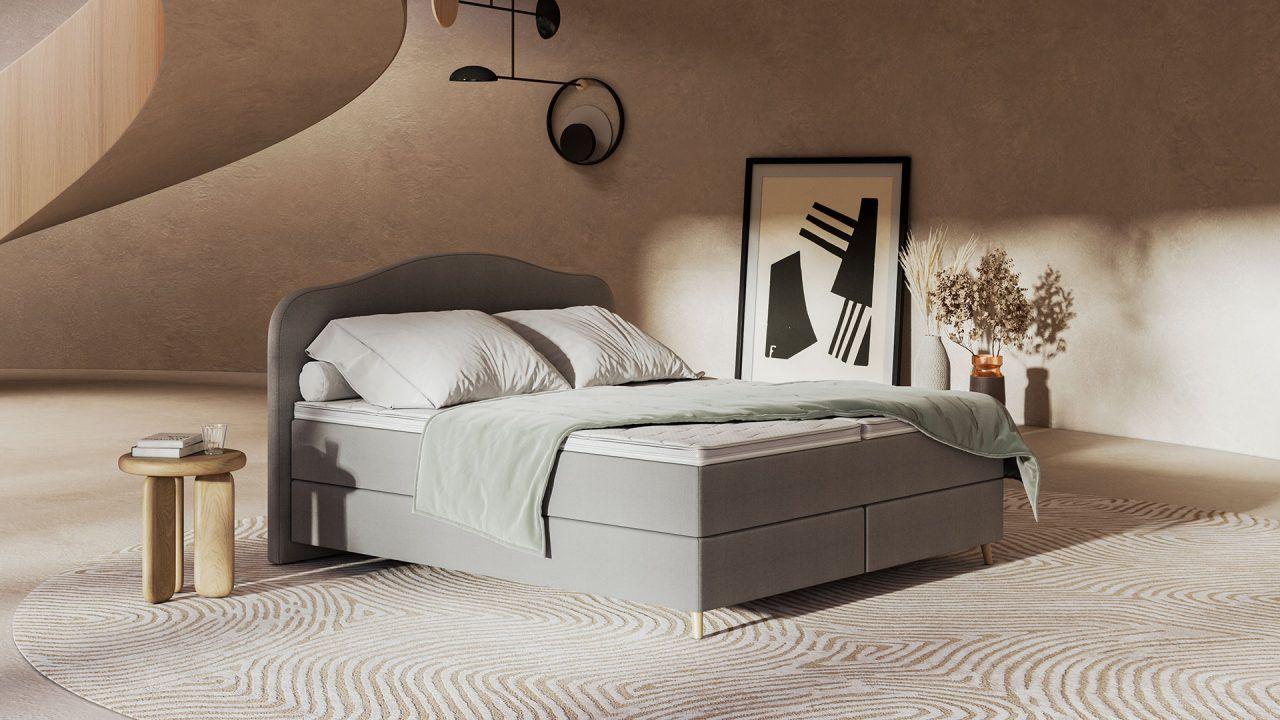 Graues Boxspringbett mit dunkelgrauem Kopfteil in warmem Schlafzimmer mit gebogener Holzwand, modernen Pendelleuchten, gerahmter Kunst und rundem Teppich mit Wellenmuster.