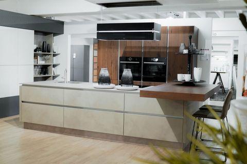 Moderne Küche mit beiger Kochinsel, Holzschränken und eingebauten schwarzen Geräten in offener Wohnraumgestaltung.